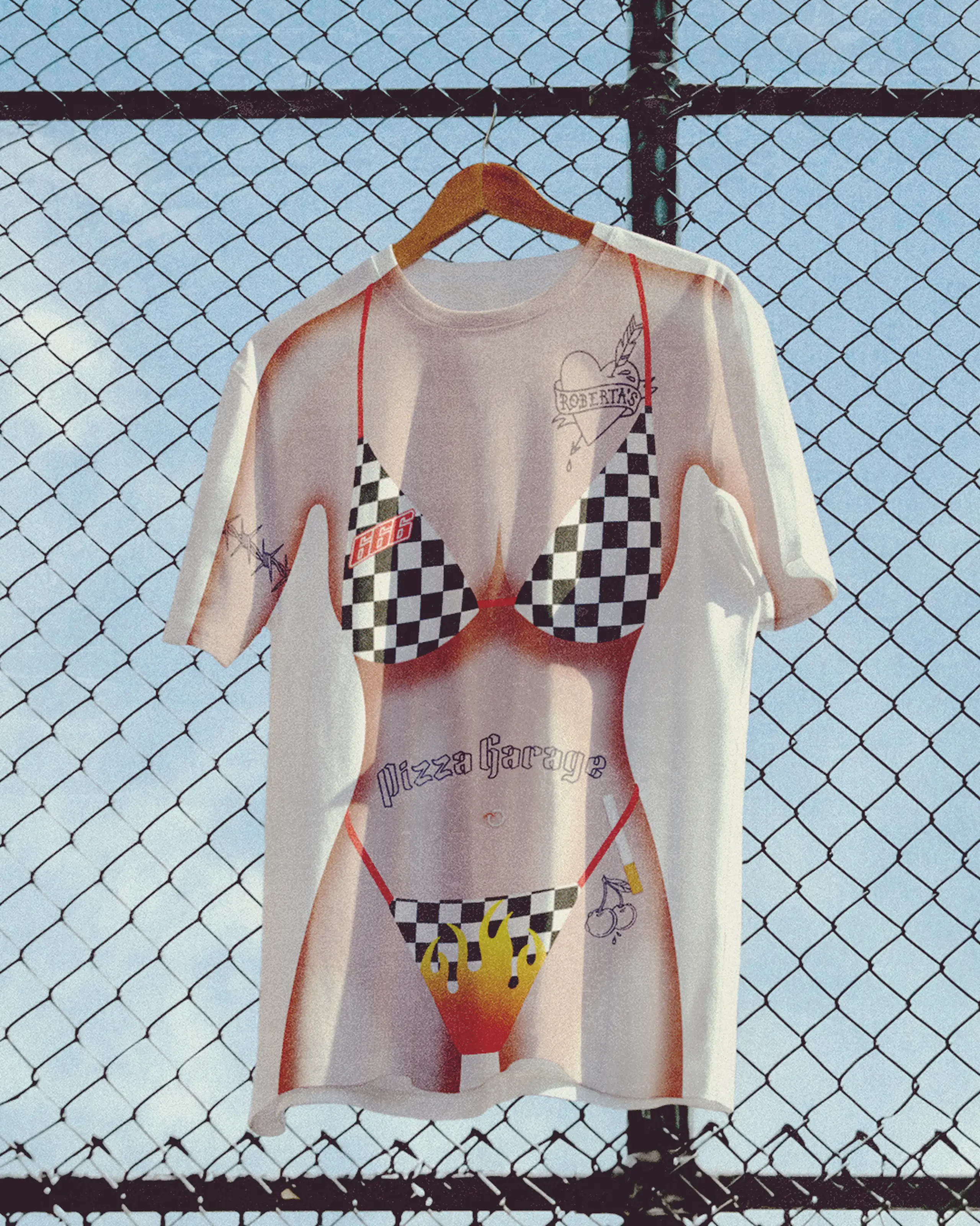 T-shirt with a graphic of a bikini and tattoos, hanging on a fence against a blue sky.