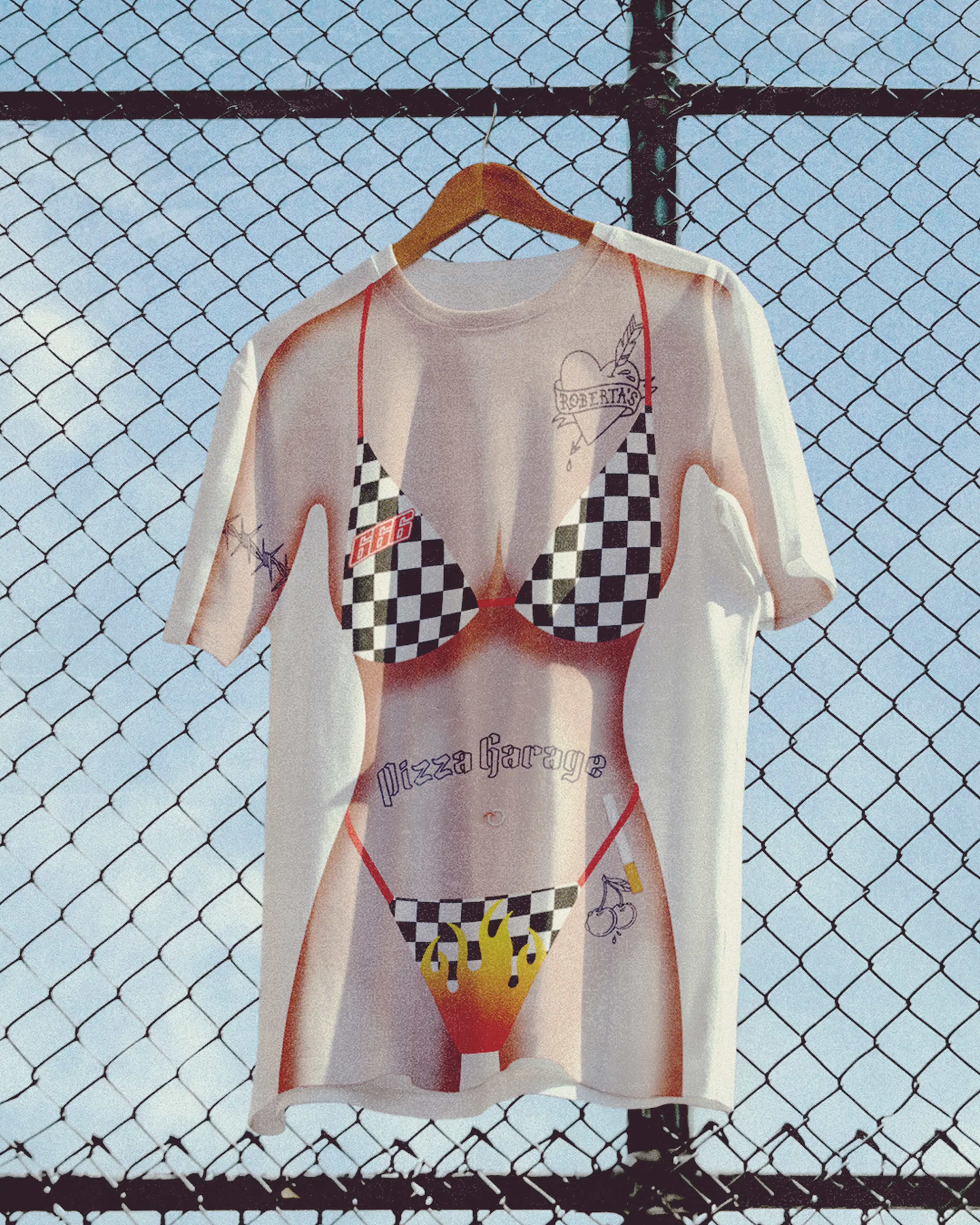T-shirt with a graphic of a bikini and tattoos, hanging on a fence against a blue sky.