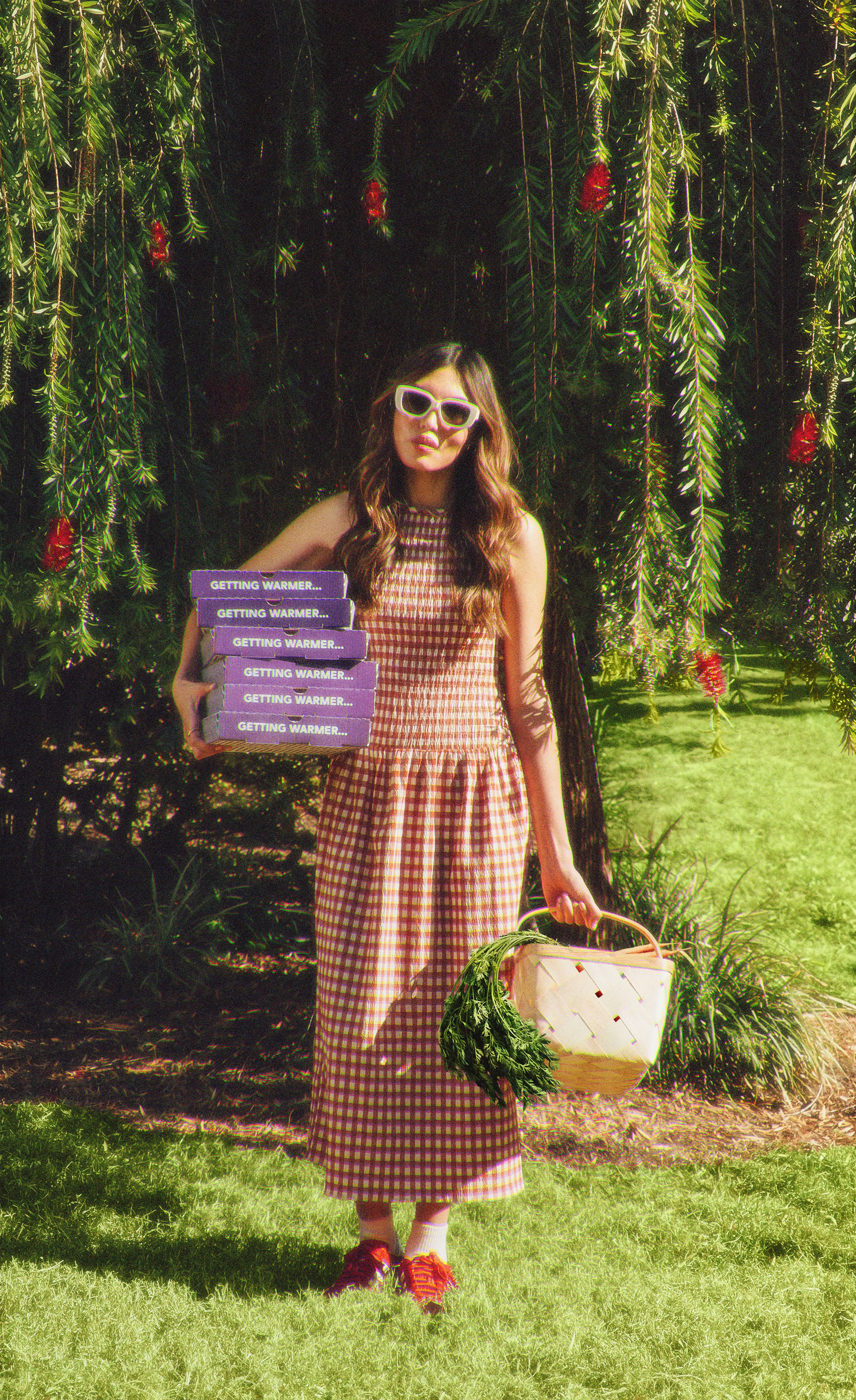 Girl going to a picnic with boxes of insomnia cookies in one hand and a picnic basket in the other