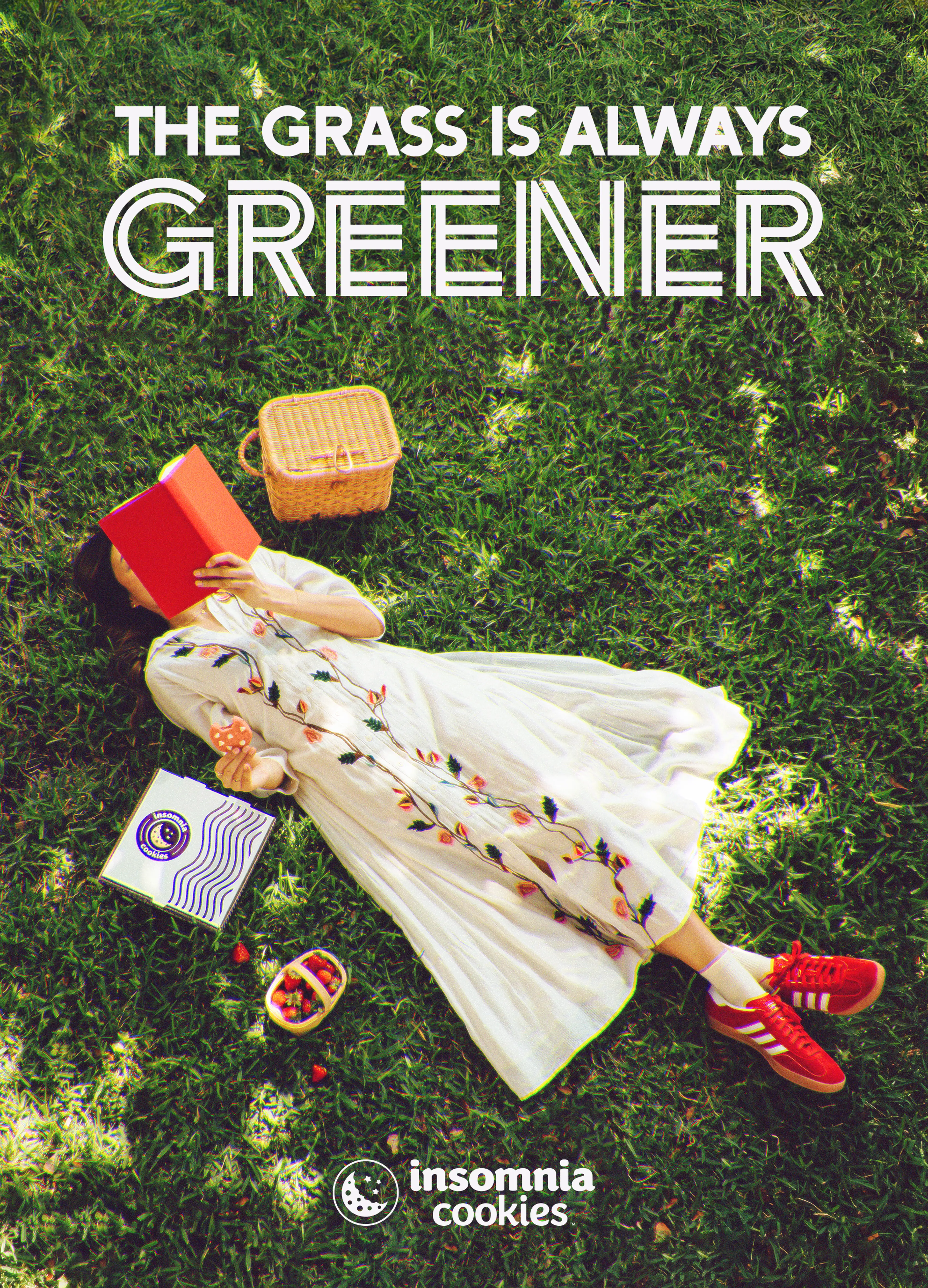 Girl laying on the grass reading a book eating insomnia cookies
