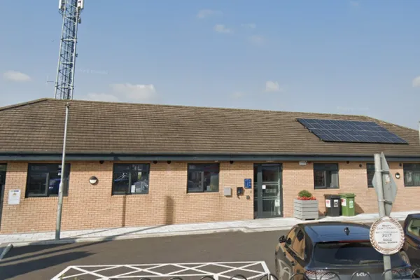 Brick building with solar panels on the roof, a large antenna, and cars parked in front under a clear blue sky.