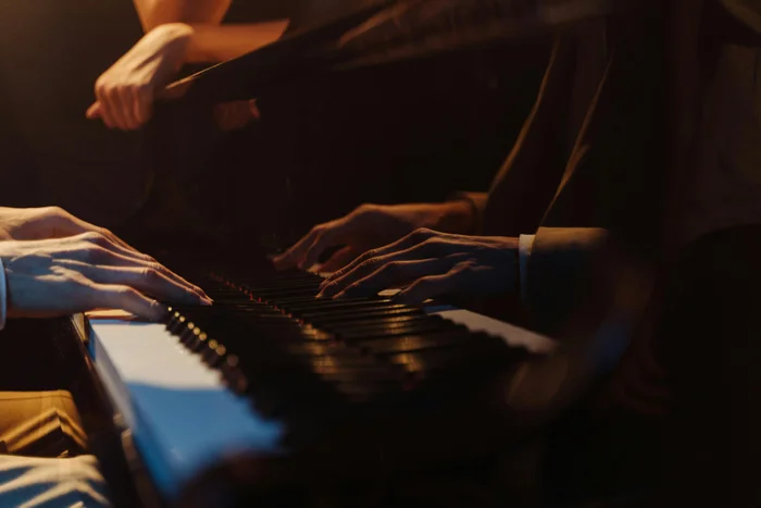 Hands playing a piano in warm lighting, with reflections visible on the glossy surface.