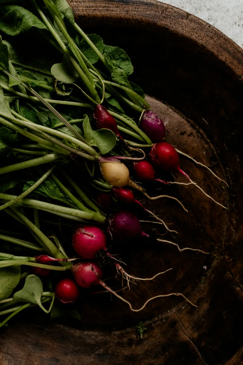 A bunch of freshly harvested radishes with green leaves, displayed in a rustic wooden bowl.