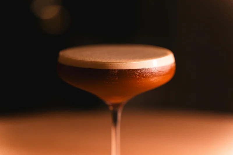 Close-up of a classic cocktail in a coupe glass, dark bar background — Gilt, Mayfair London, Studio Cicely hospitality web design