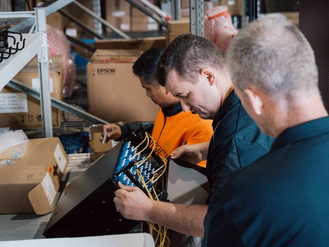Three SHC team members inspecting a fibre patch panel