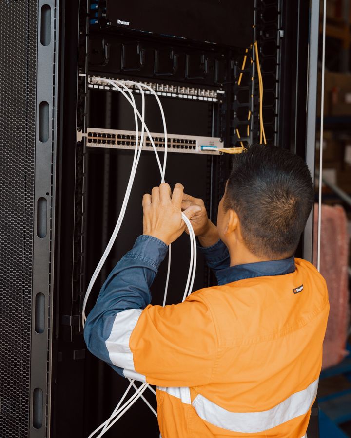 Team member in hi-vis running patch cables through a data rack