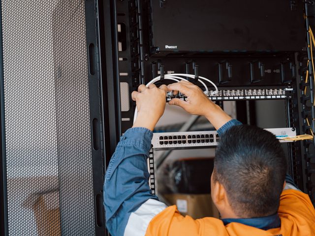 SHC team member in hi-vis patching network cables in a data rack