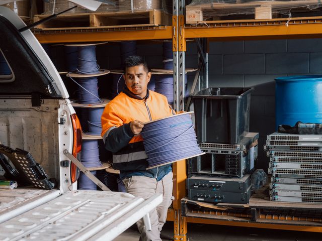 SHC team member in hi-vis carrying a reel of cable from a work ute