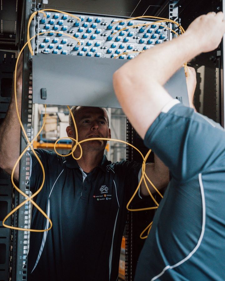 Two SHC team members installing a fibre panel in a data rack