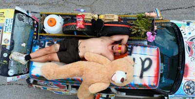 Teilnehmer beim Pothole Rodeo liegt gemeinsam mit Lenny dem Maskottchen auf dem Autodach und entspannt