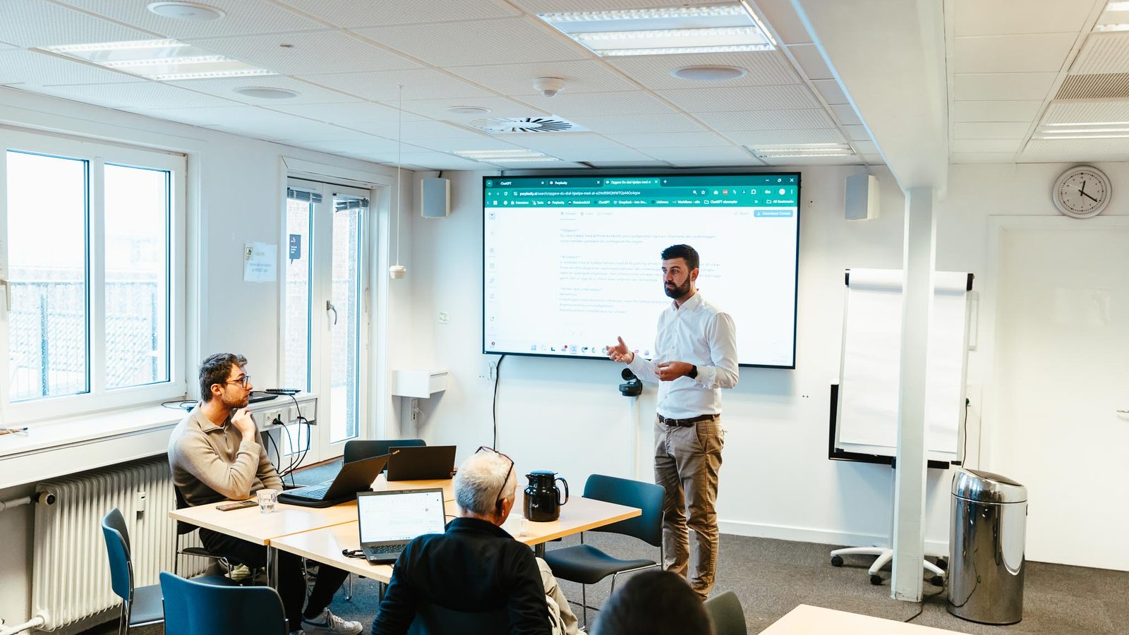 Jacob faciliterer en workshop om AI orchestratoren med kolleger og laptops i et lyst mødelokale