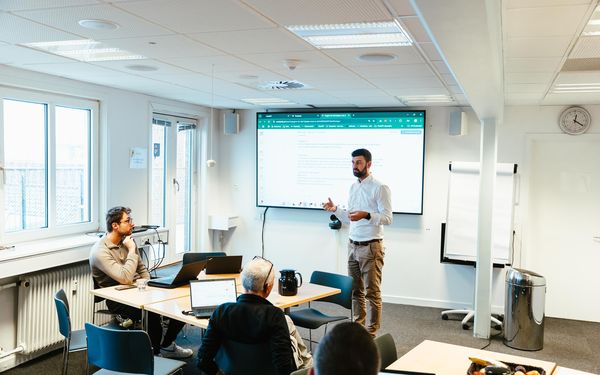 Jacob faciliterer en workshop om AI orchestratoren med kolleger og laptops i et lyst mødelokale