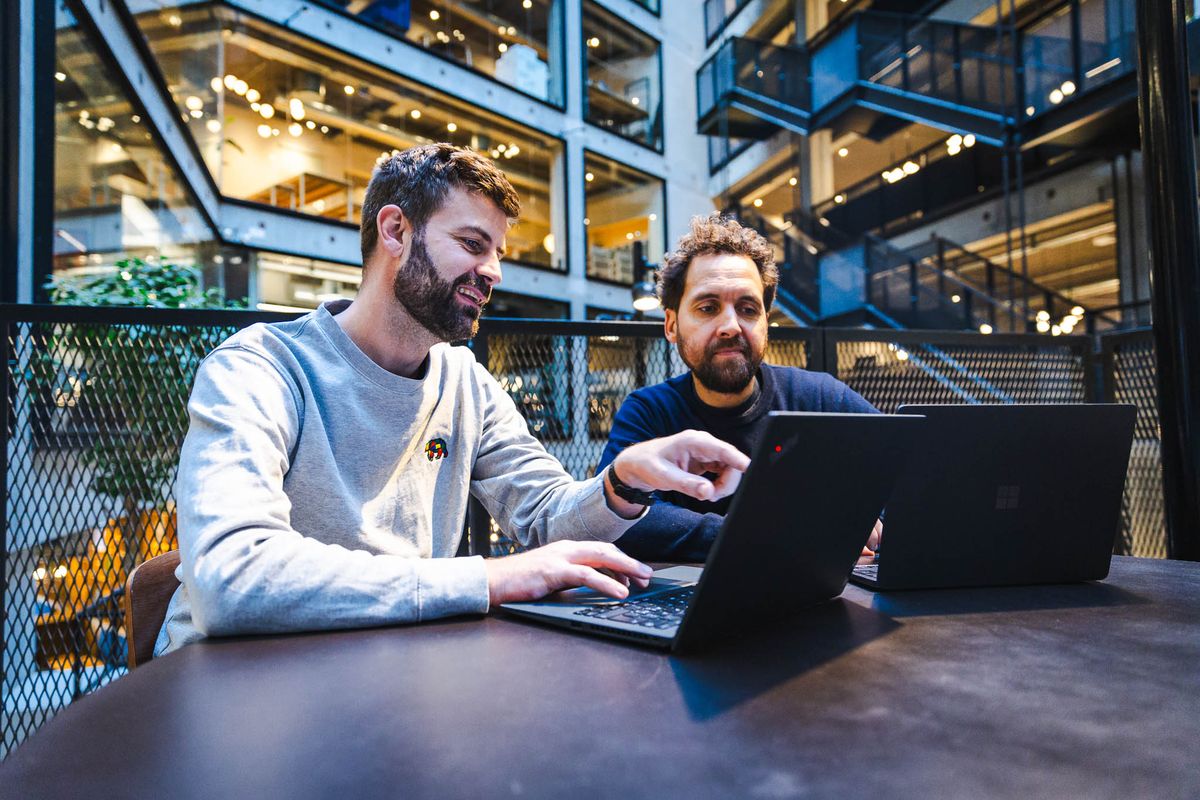 Jacob og kollega samarbejder ved laptops om arbejdsflow til Claude kursus i moderne kontor