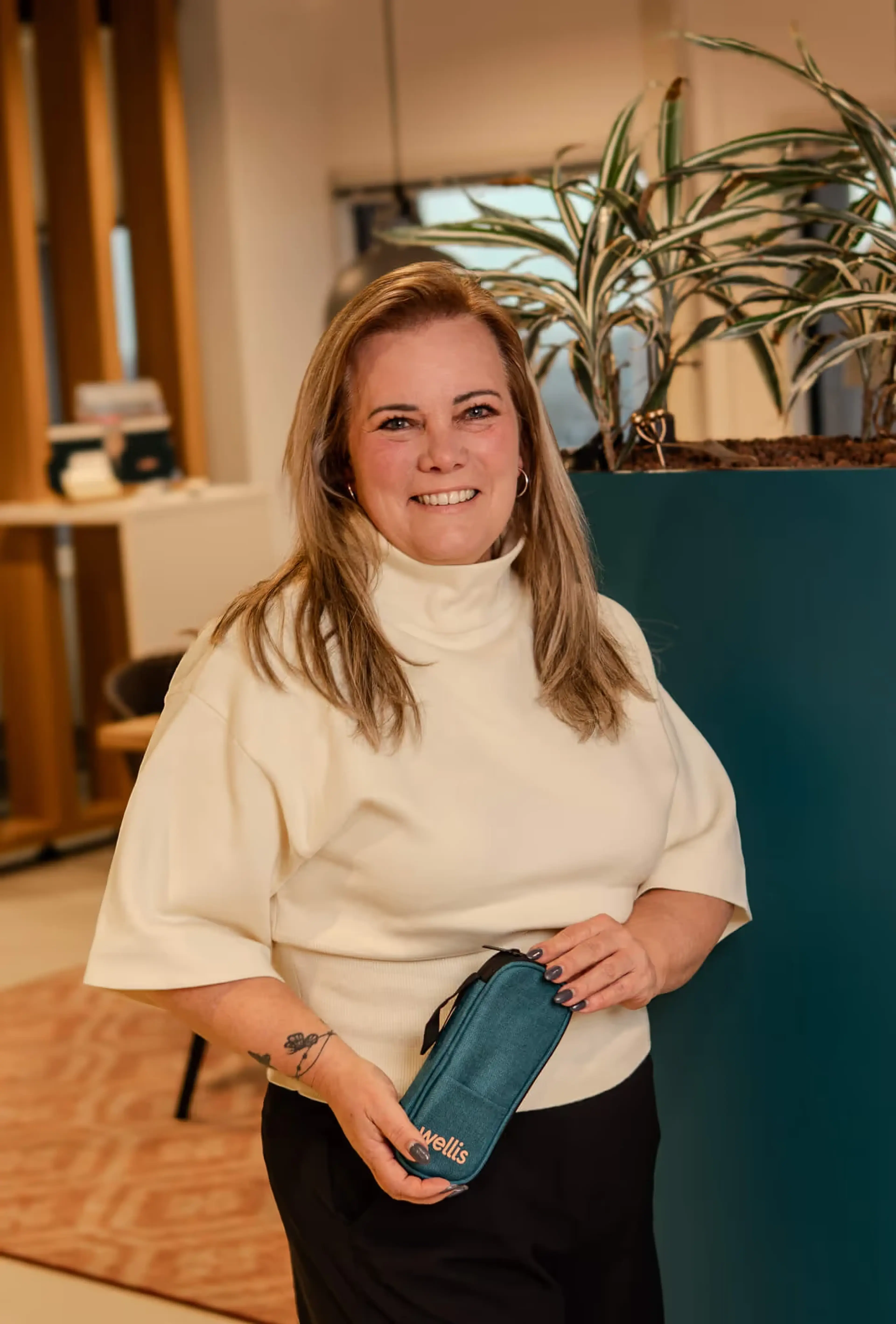 Eveline Engels staat lachend in het Wellis-kantoor met een blauwgroen Wellis-etui in haar handen.