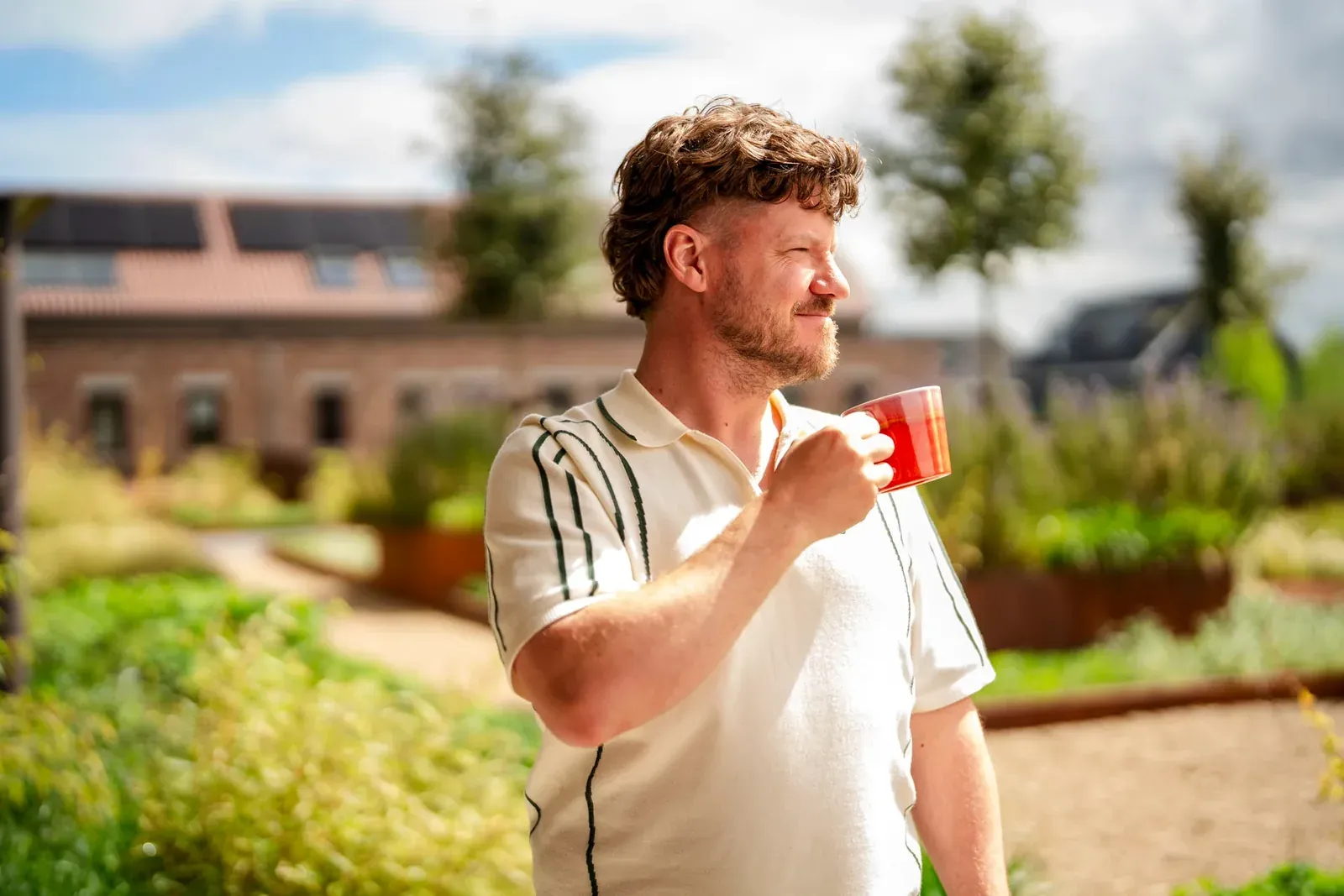 Man drinkt buiten uit een rode mok in een groene tuin