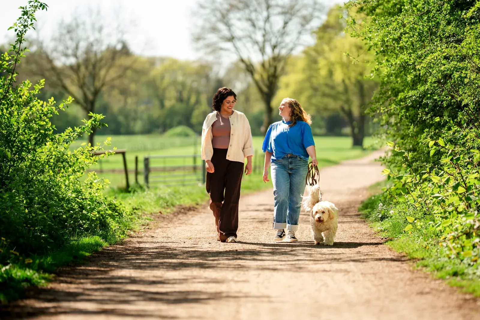 Twee vrouwen wandelen met een witte hond over een landweg