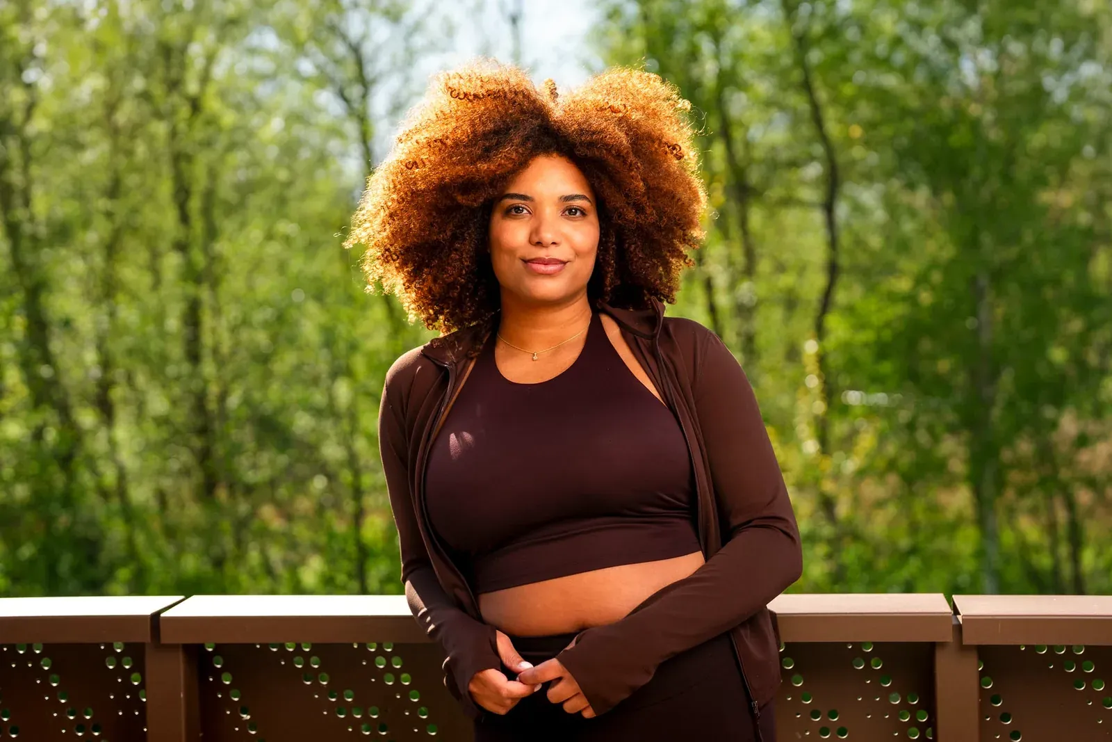 Vrouw in sportkleding staat buiten op een terras tussen de bomen