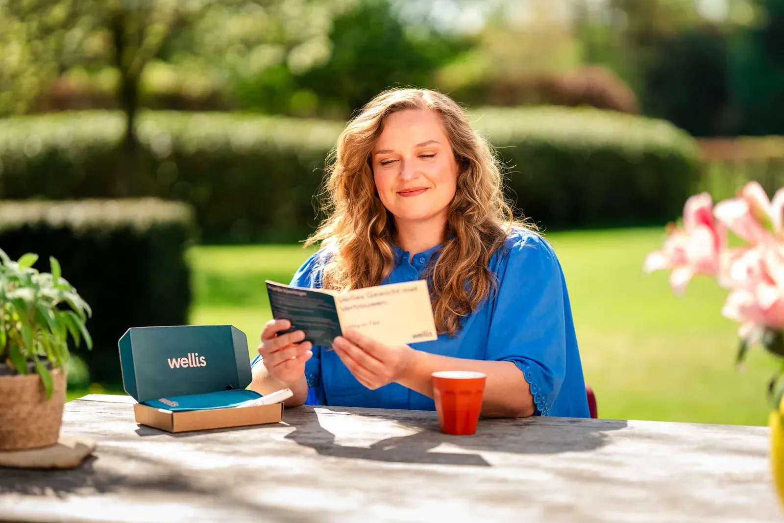 Vrouw leest buiten aan tafel een bijsluiter, met een Wellis-doos ernaast