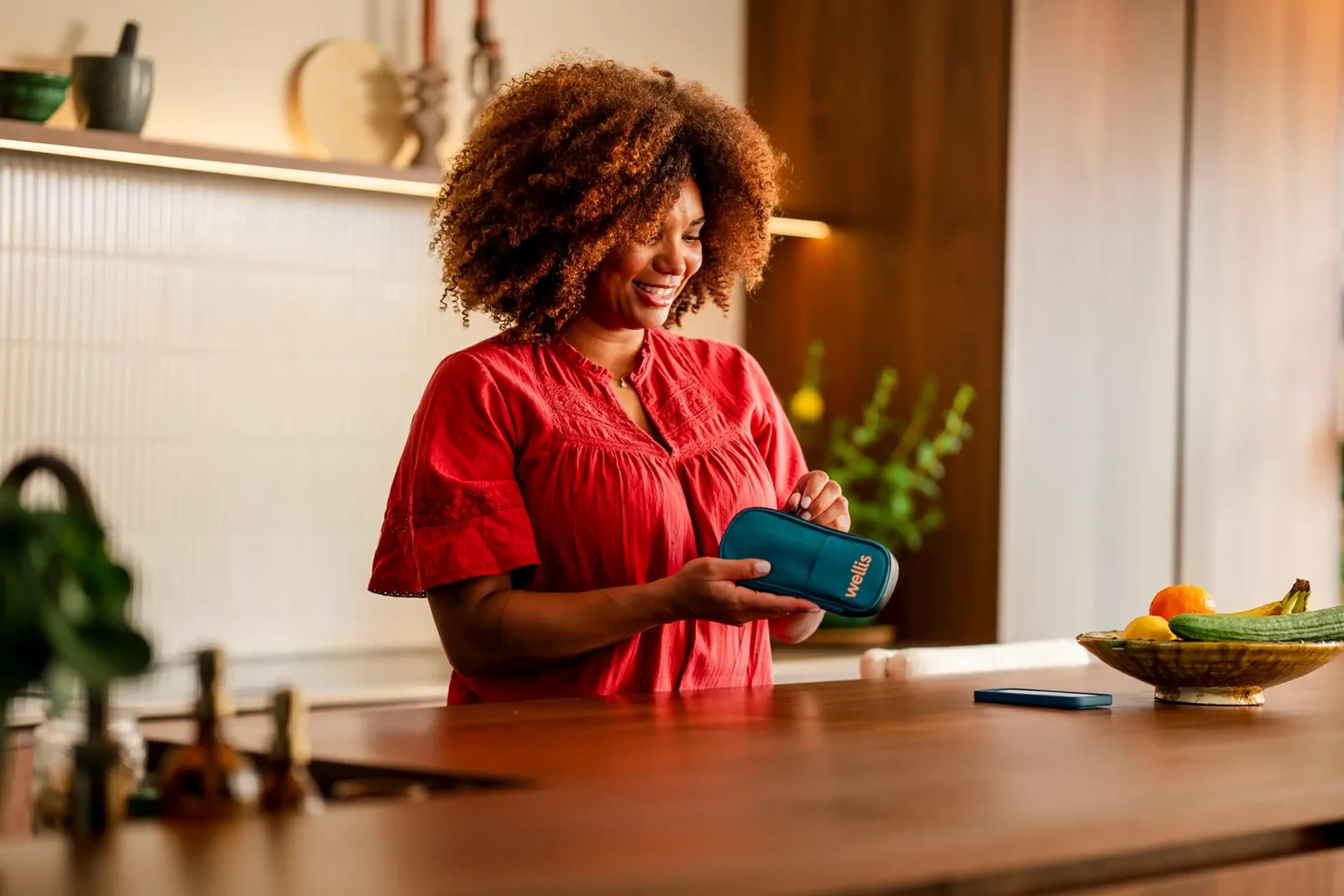 Lachende vrouw in een rode blouse houdt in de keuken een pen-etui vast