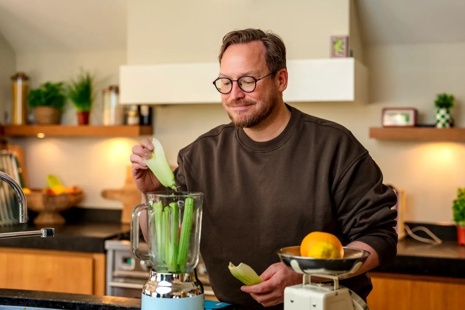 Man met bril snijdt groente naast een blender in de keuken