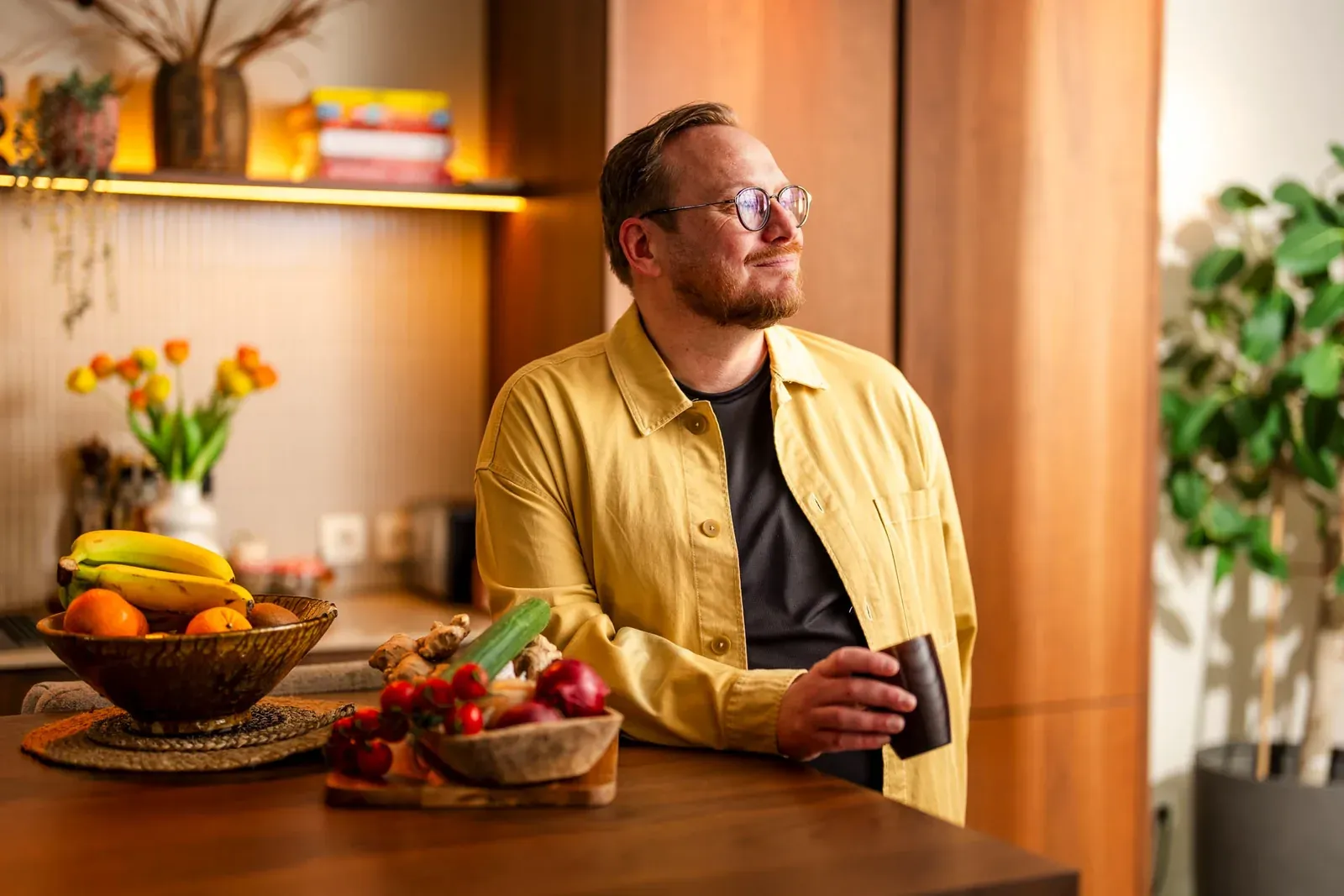 Man met bril in een geel overhemd staat aan de keukentafel met schalen fruit