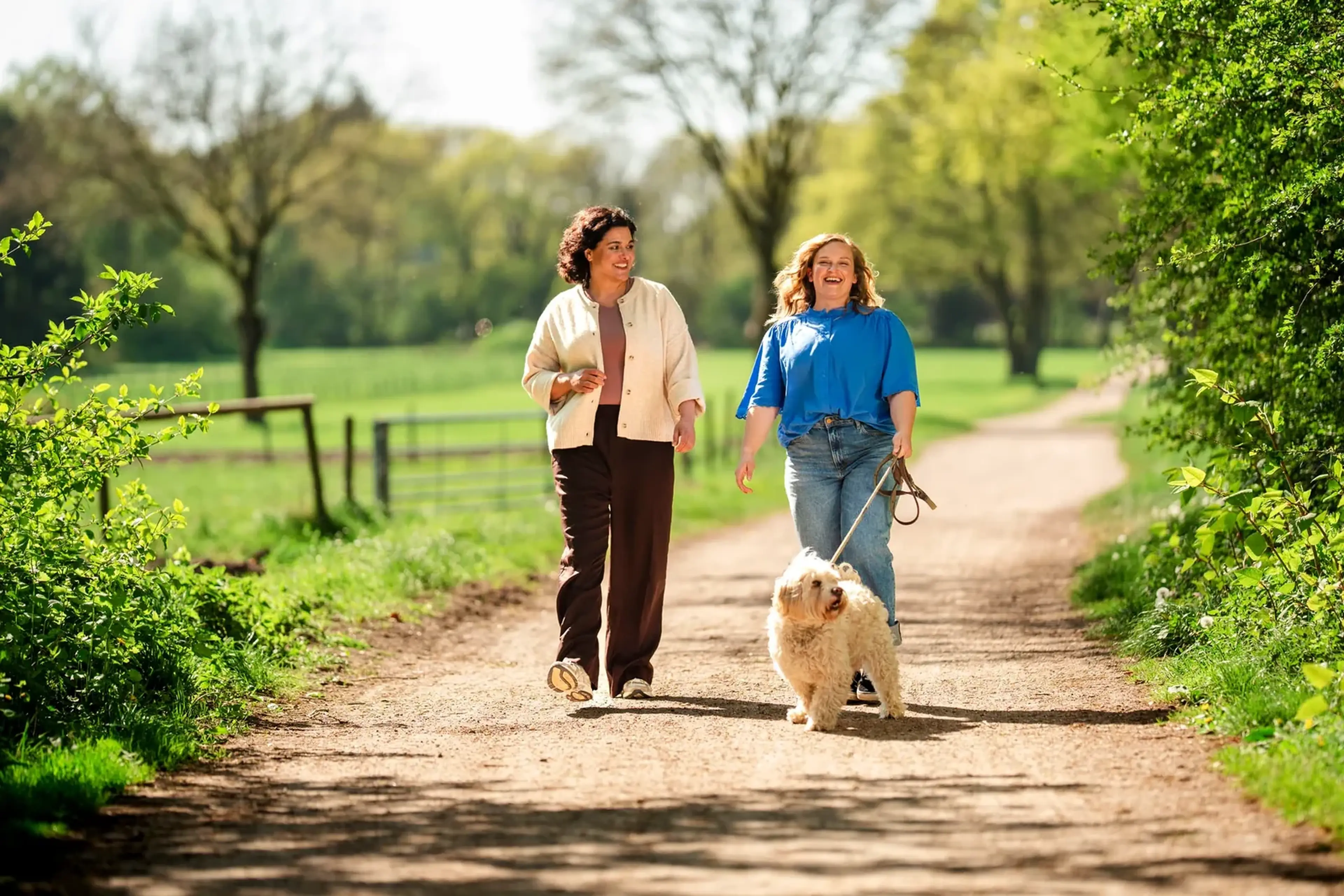 Twee vrouwen wandelen met een lichte hond over een zonnige landweg
