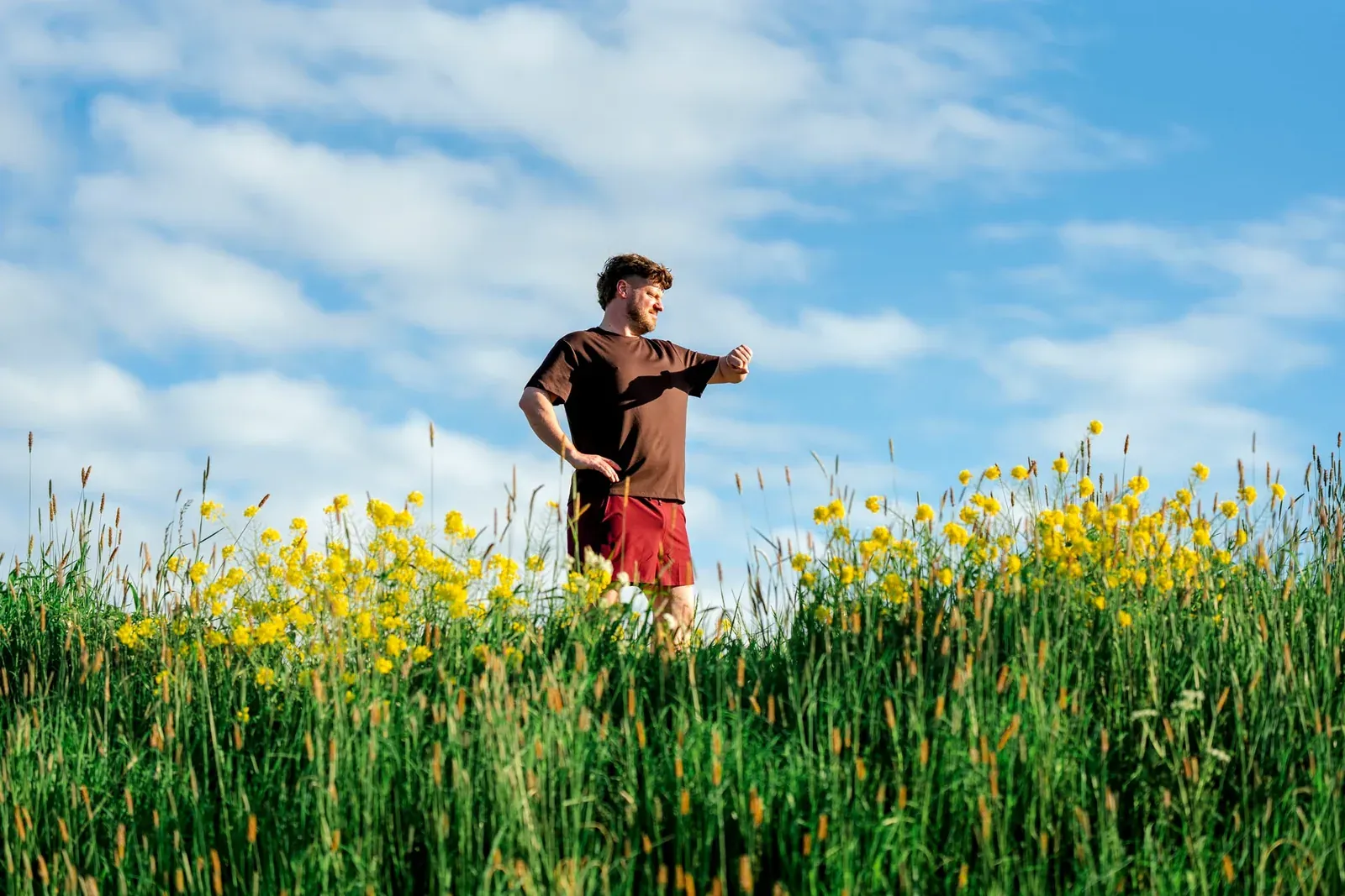 Man staat in een veld met gele bloemen onder een blauwe lucht