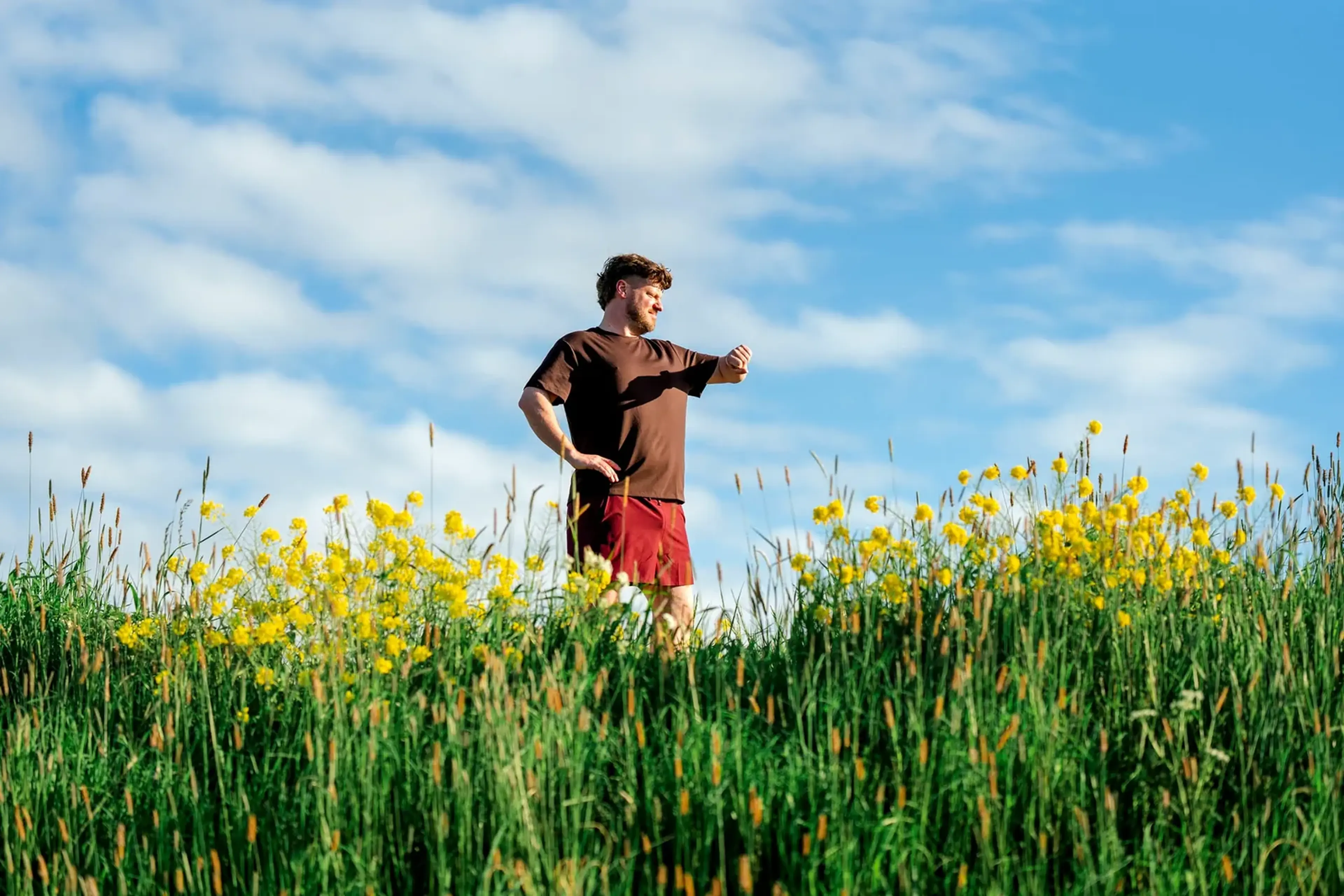 Man staat in een veld met gele bloemen onder een blauwe lucht