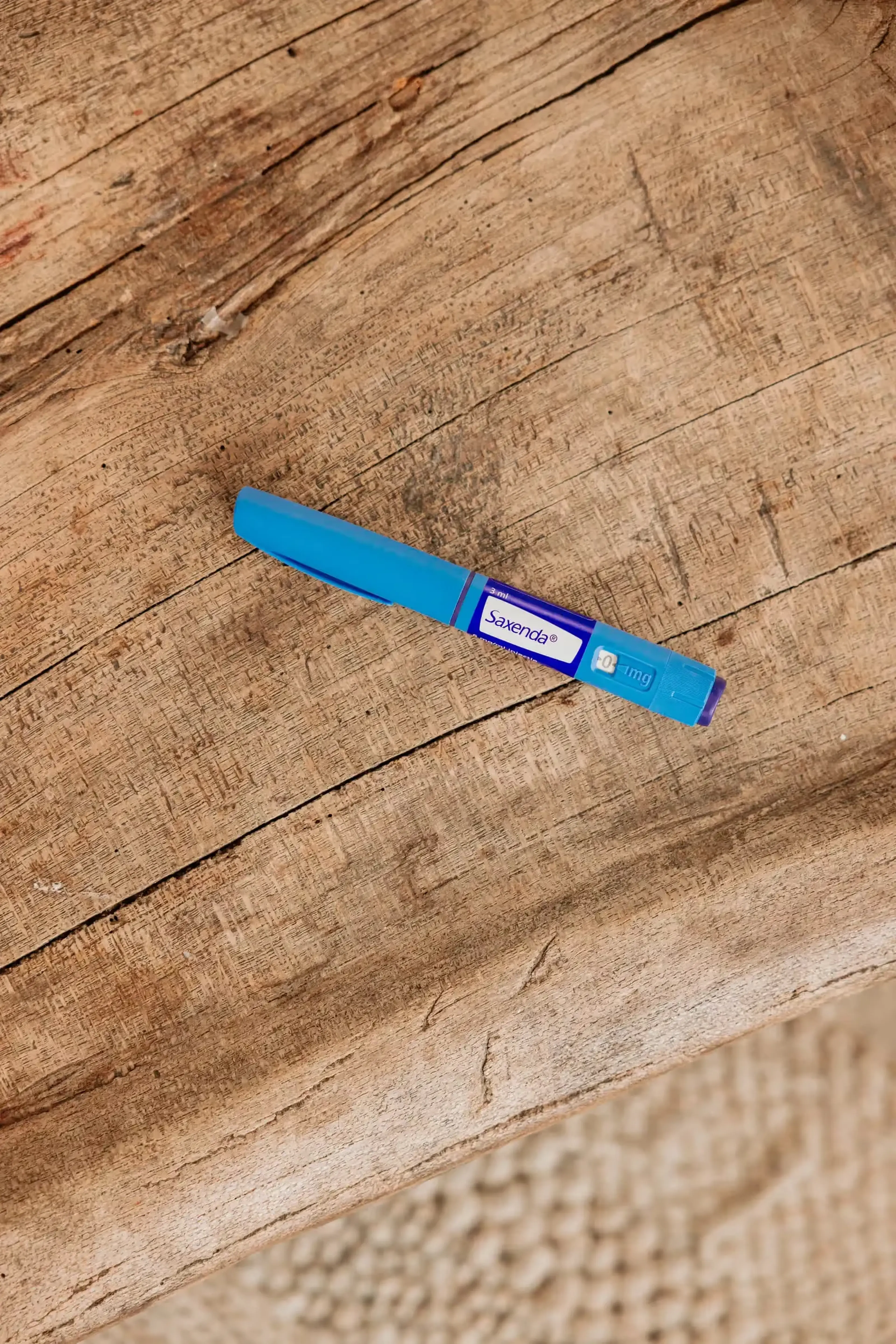 Blauwe Saxenda-injectiepen met doseerknop ligt op een houten tafel
