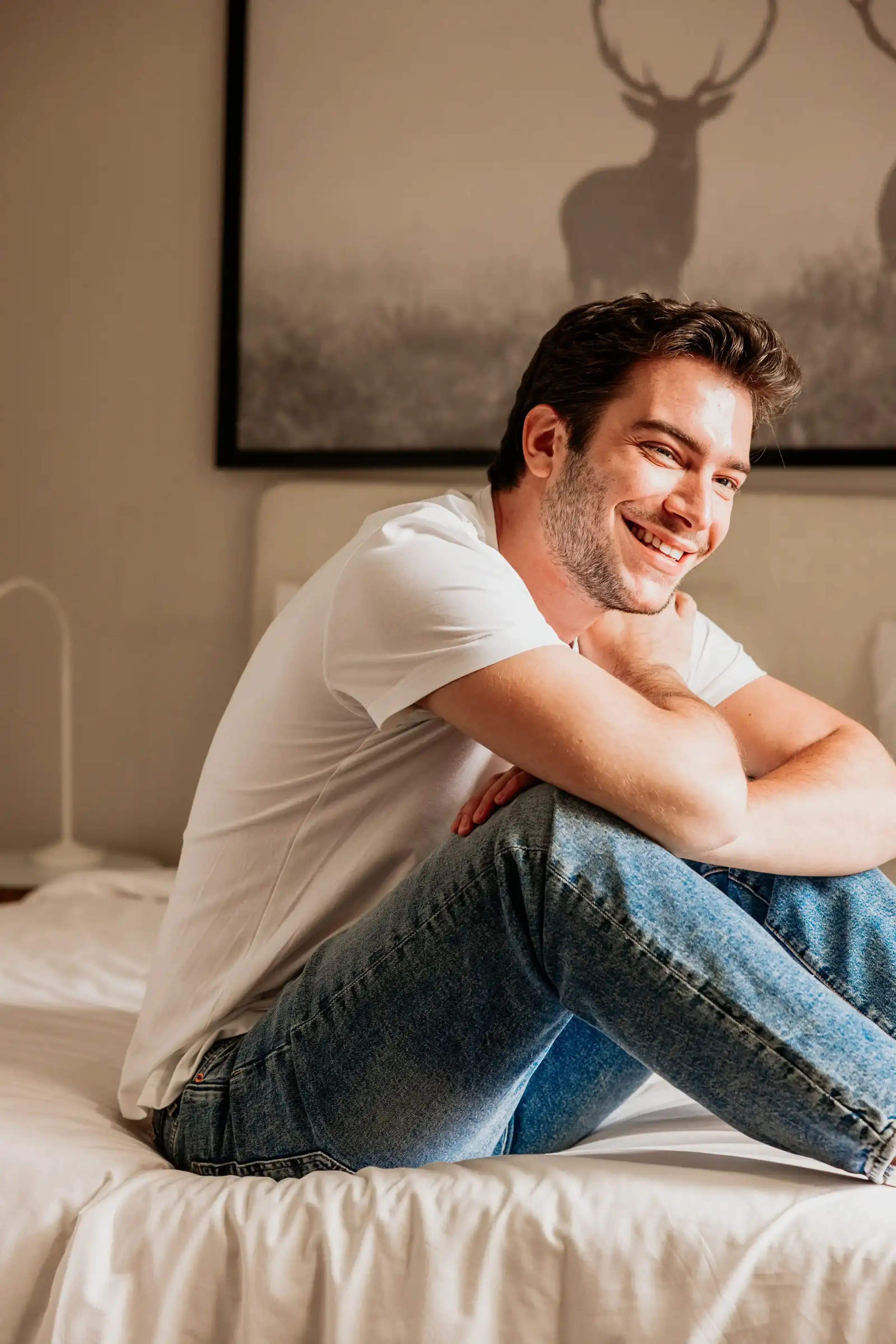 Lachende man in een wit T-shirt zit ontspannen op zijn bed – afvallen met Ozempic