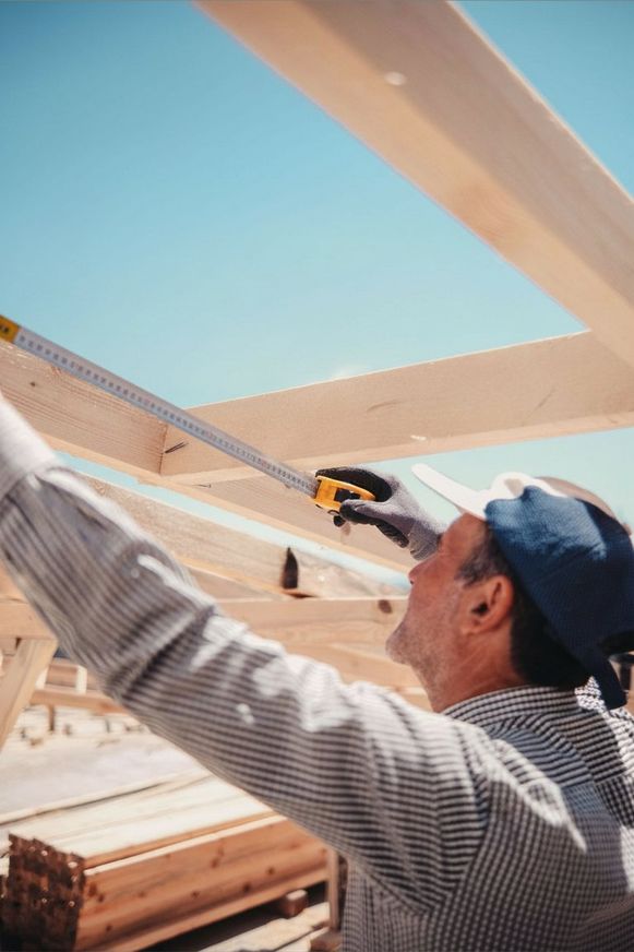 Handwerker misst einen Dachbalken mit dem Zollstock gegen den Himmel