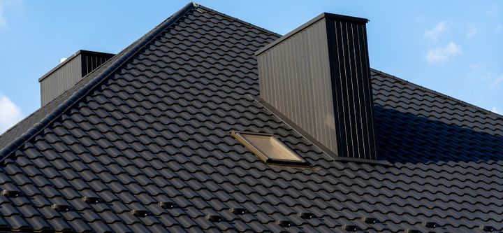 Anthrazitfarbenes Ziegeldach mit Gaube, darueber ein Streifen blauer Himmel