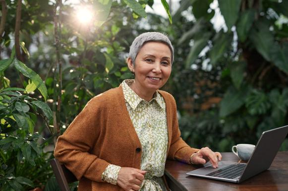 Frau mit Laptop zwischen Pflanzen im Gegenlicht