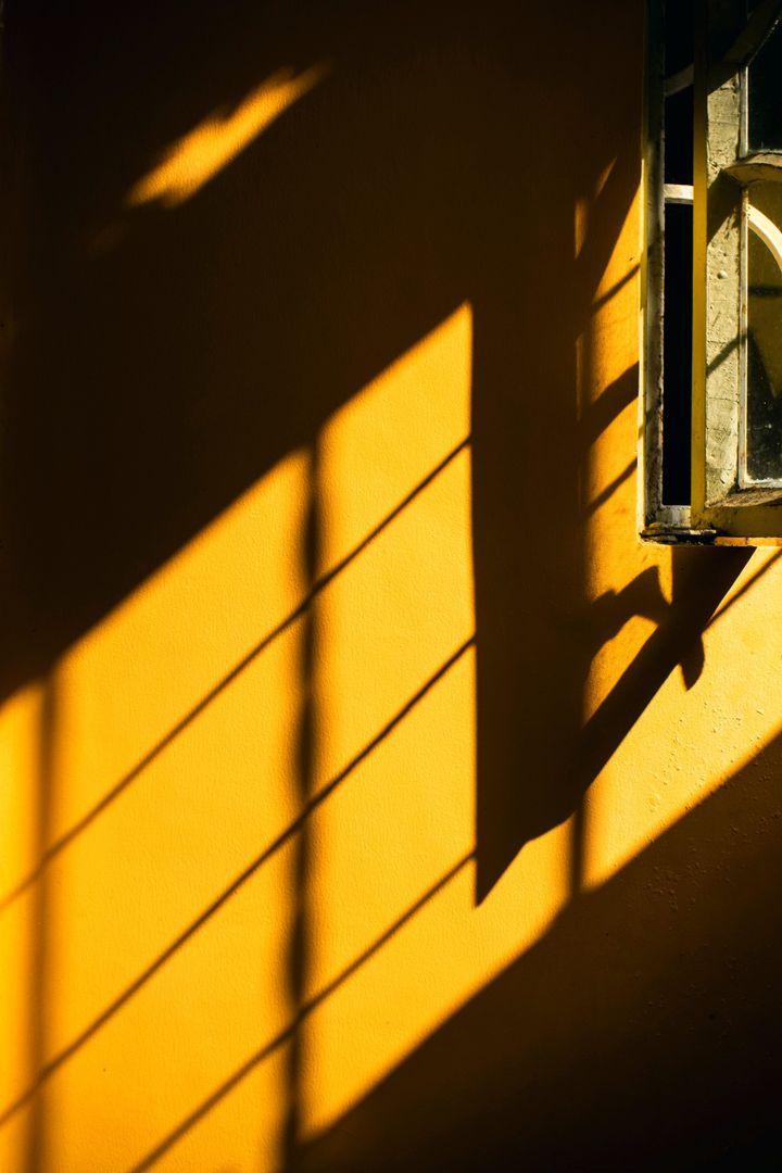 Goldgelbe Wand mit offenem Fenster und Fensterschatten