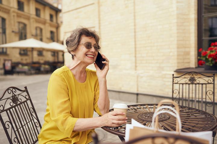 Signora sorridente al tavolino di un bar parla al telefono