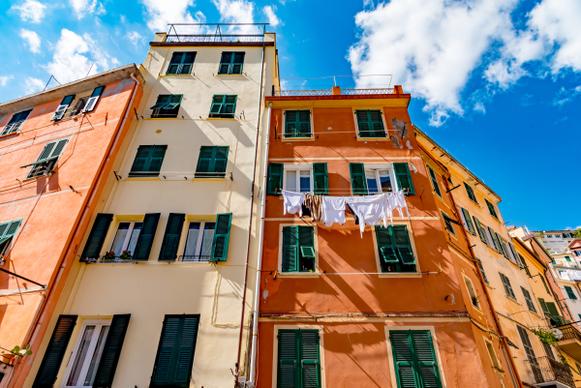 Facciate color crema e arancio con persiane verdi e panni stesi sotto un cielo azzurro