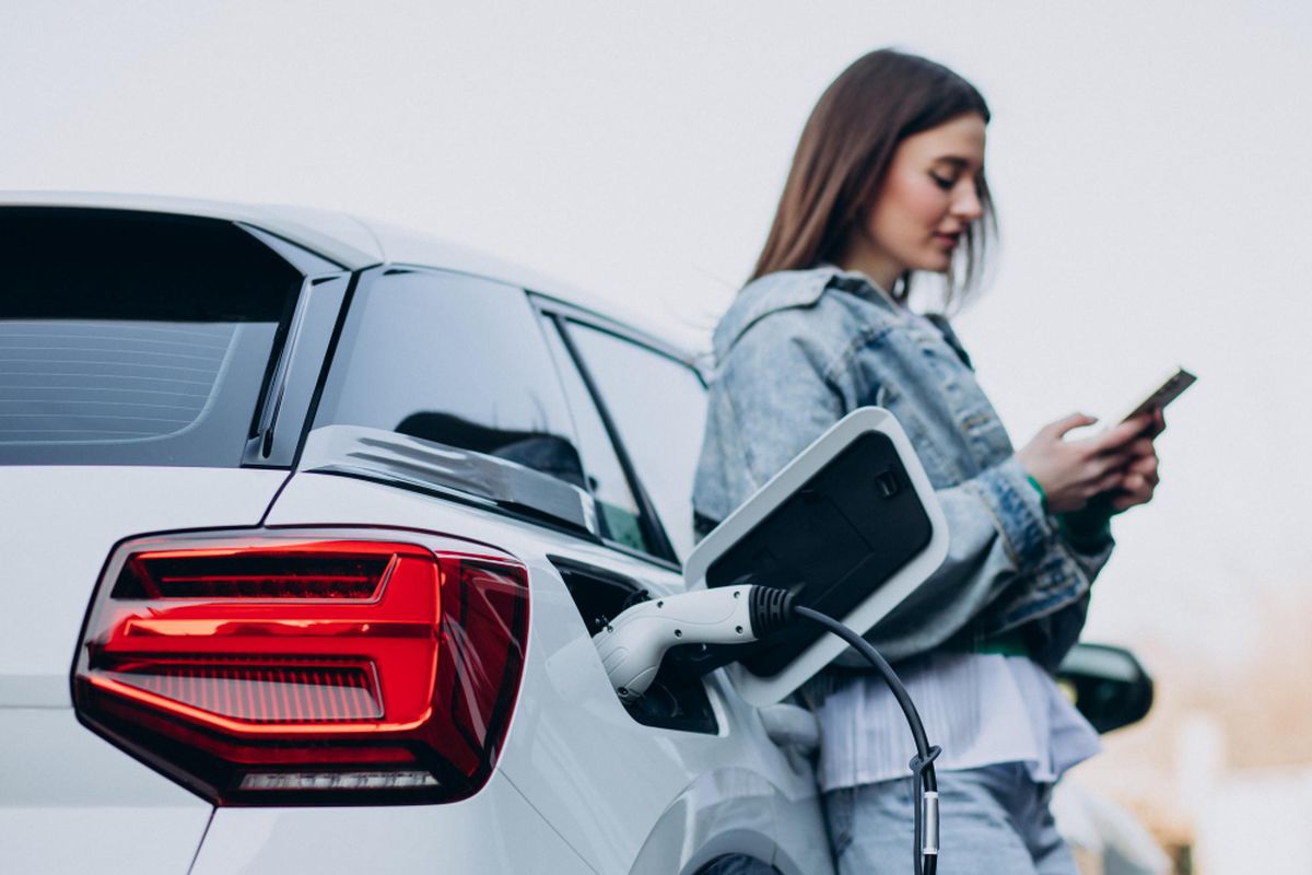 donna al telefono mentre la sua auto elettrica si ricarica