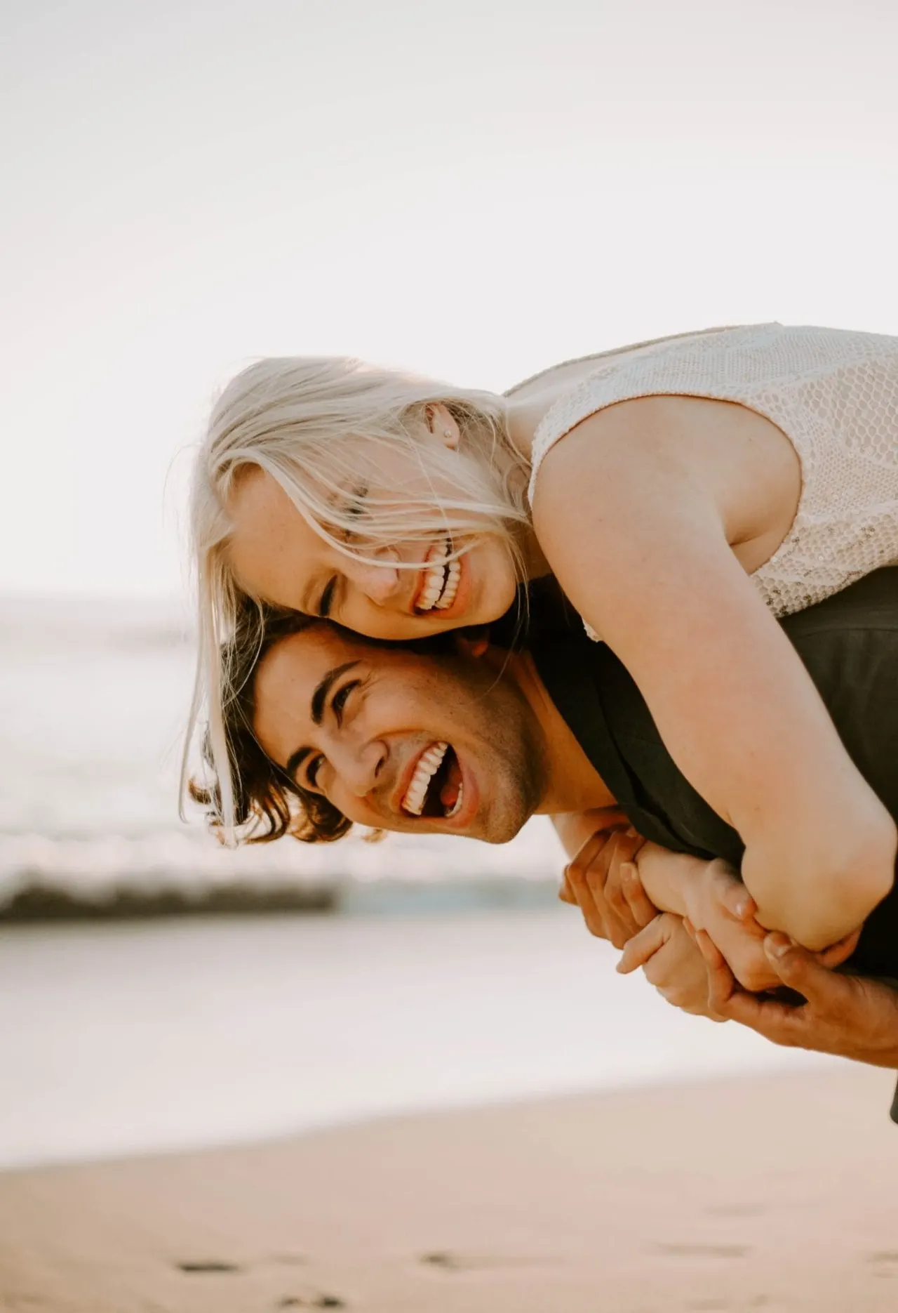 A joyful couple laughing together on the beach at sunset