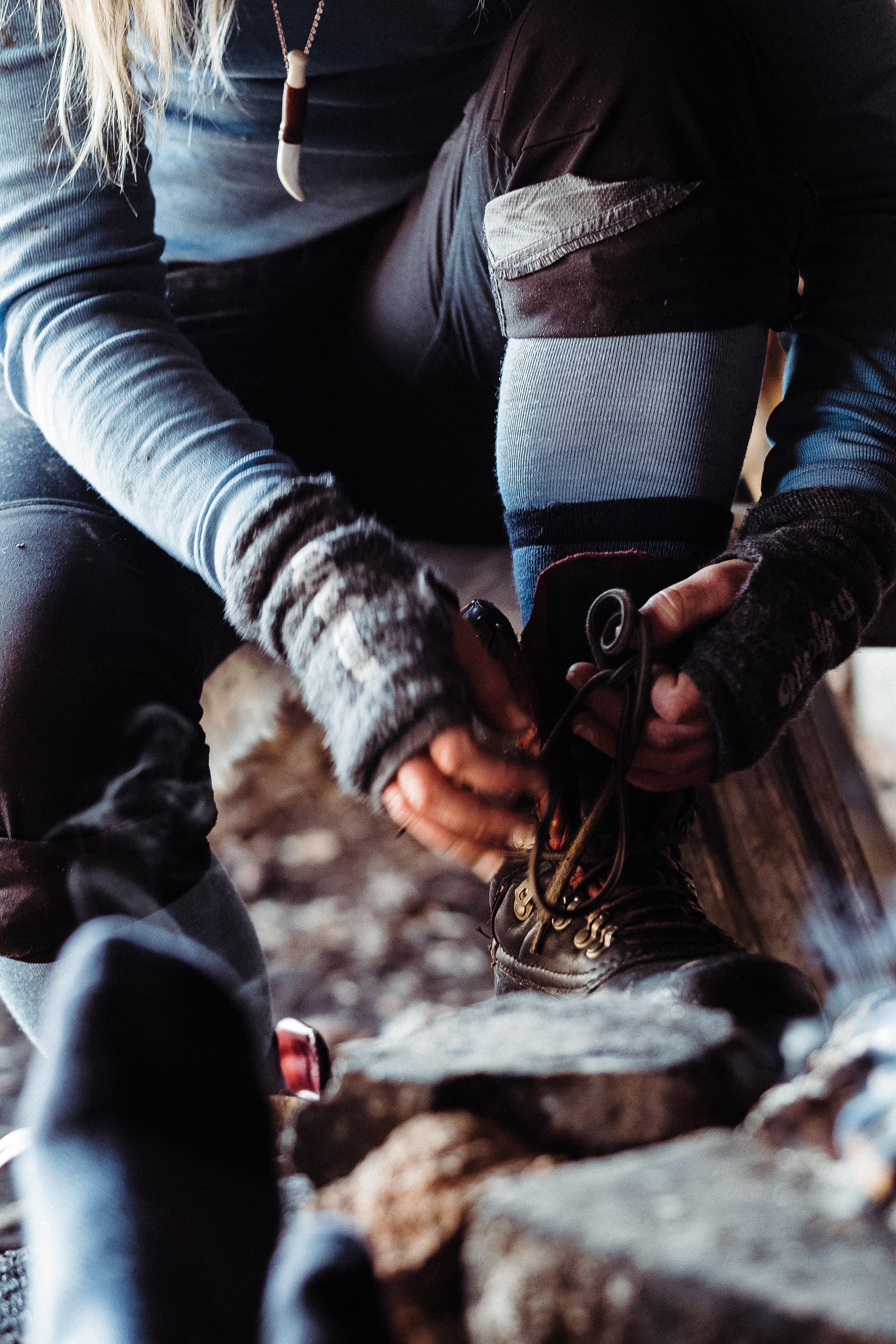 Person outdoors lacing up hiking boots, wearing hand gaiters in the color grey