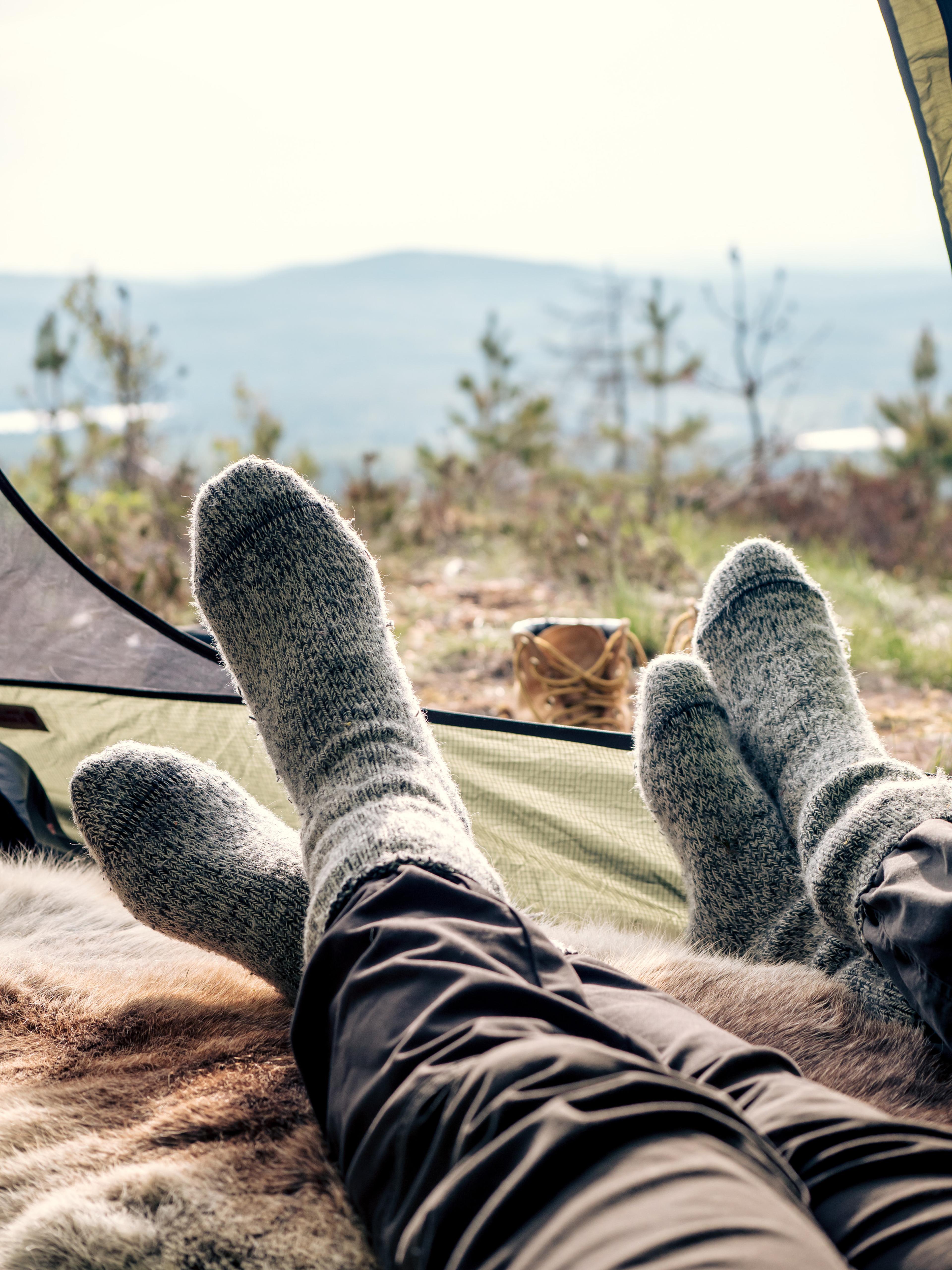 Two pairs of feet in Woolpower socks from the entry point of a tent looking out on nature
