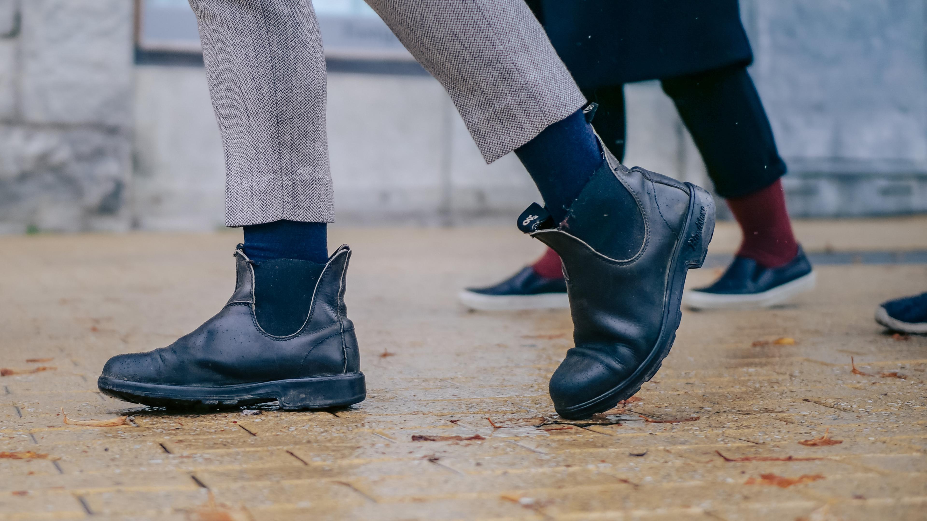 Close-up of people walking on pavement while wearing dark ankle boots and colorful socks.