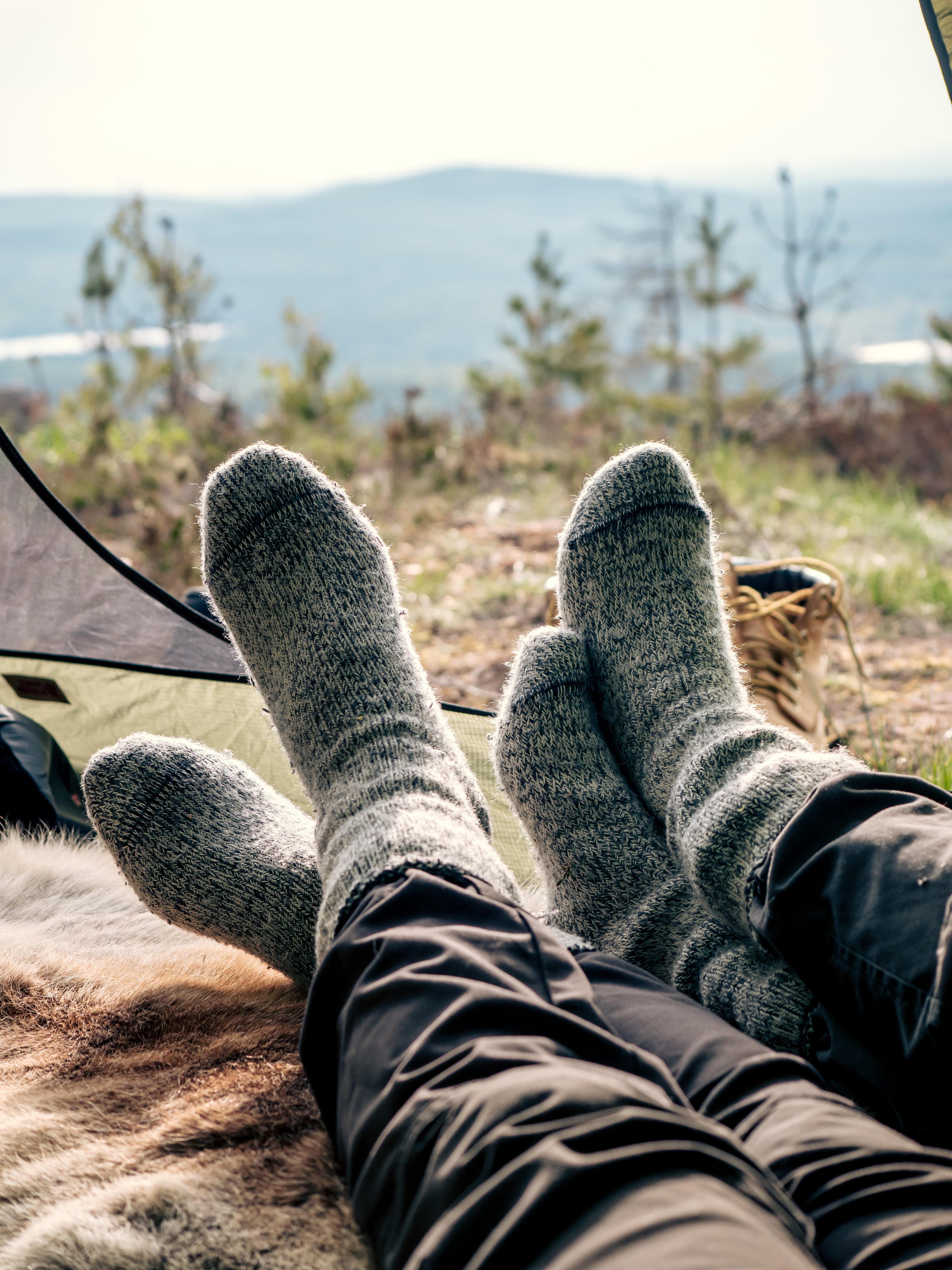 Two people wearing cozy socks relax in a tent, overlooking a scenic view of trees and distant hills.