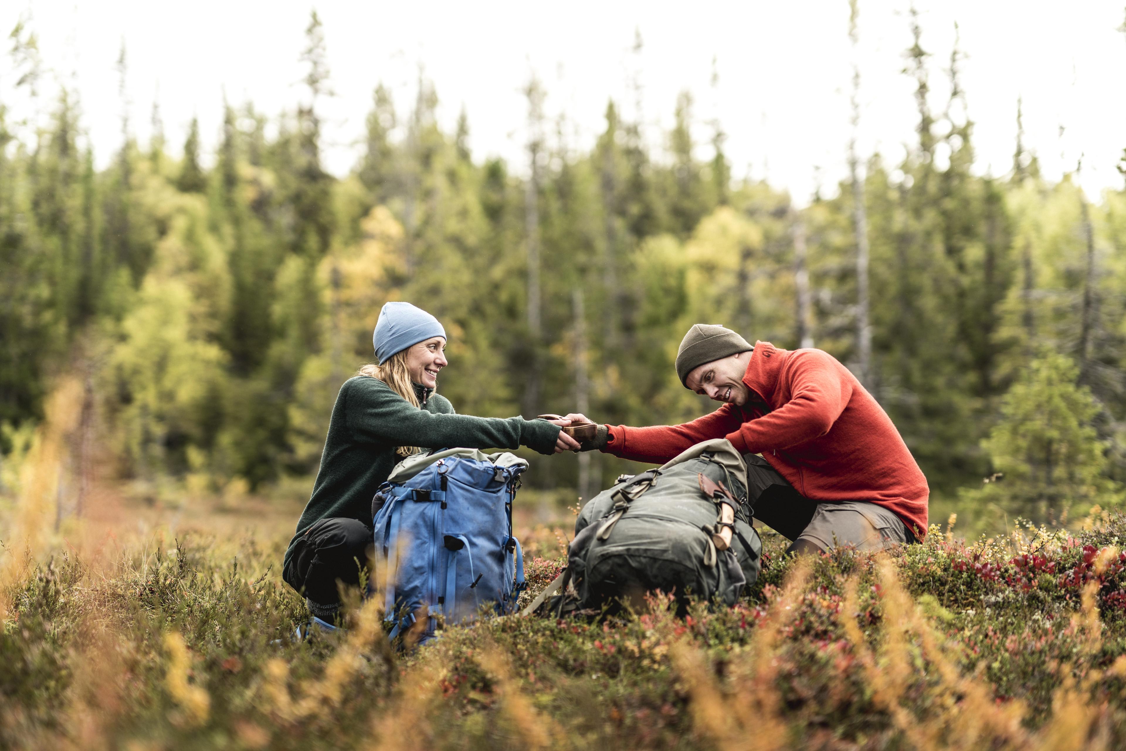 Two hikers wearing Woolpower gear, smiling and holding hands in an autumn forest.