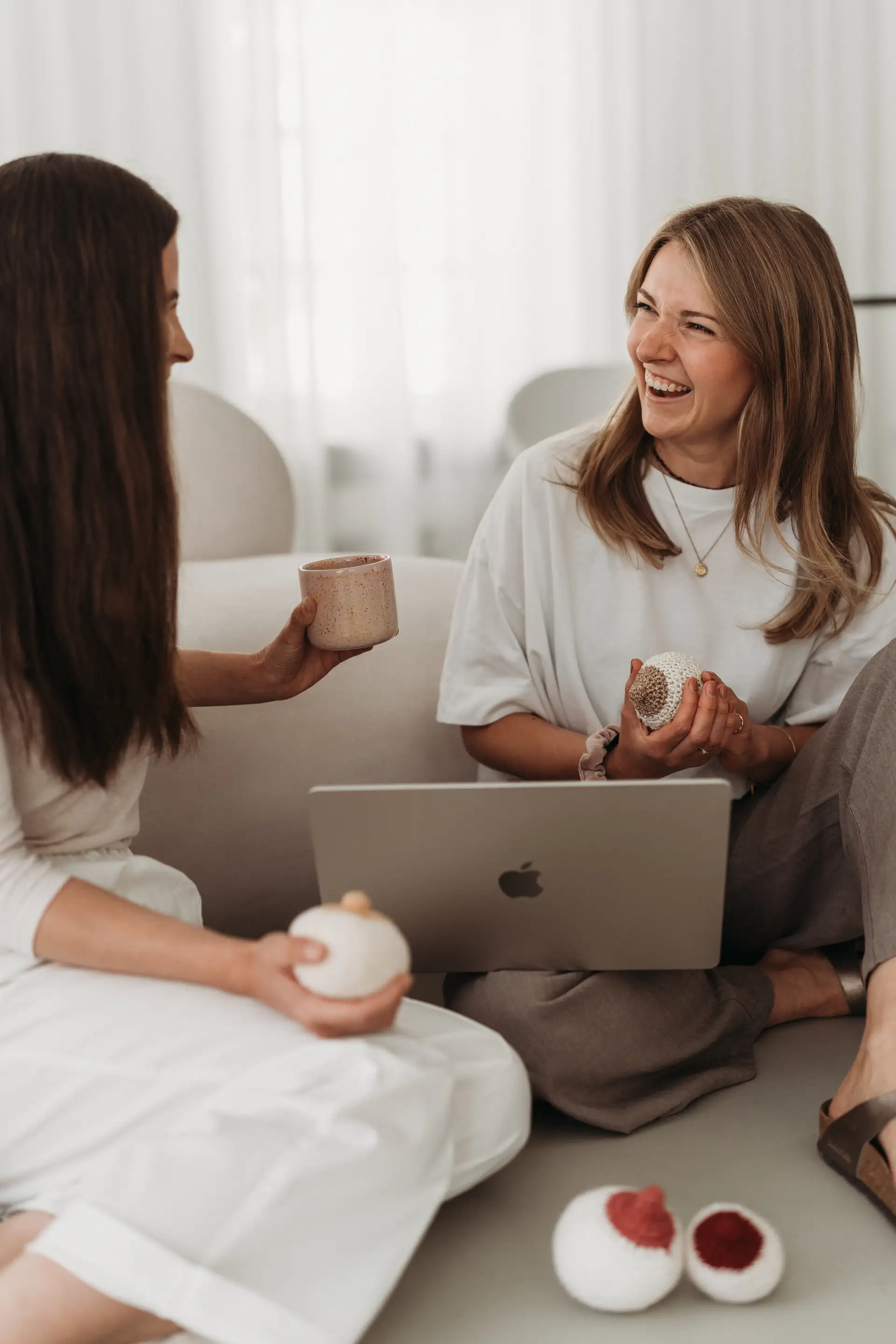 Zwei Breastkeeperinnen im Austausch auf dem Sofa mit Laptop und gehäkeltem Brust-Modell – Zusammenarbeit im Breastkeeper Institut