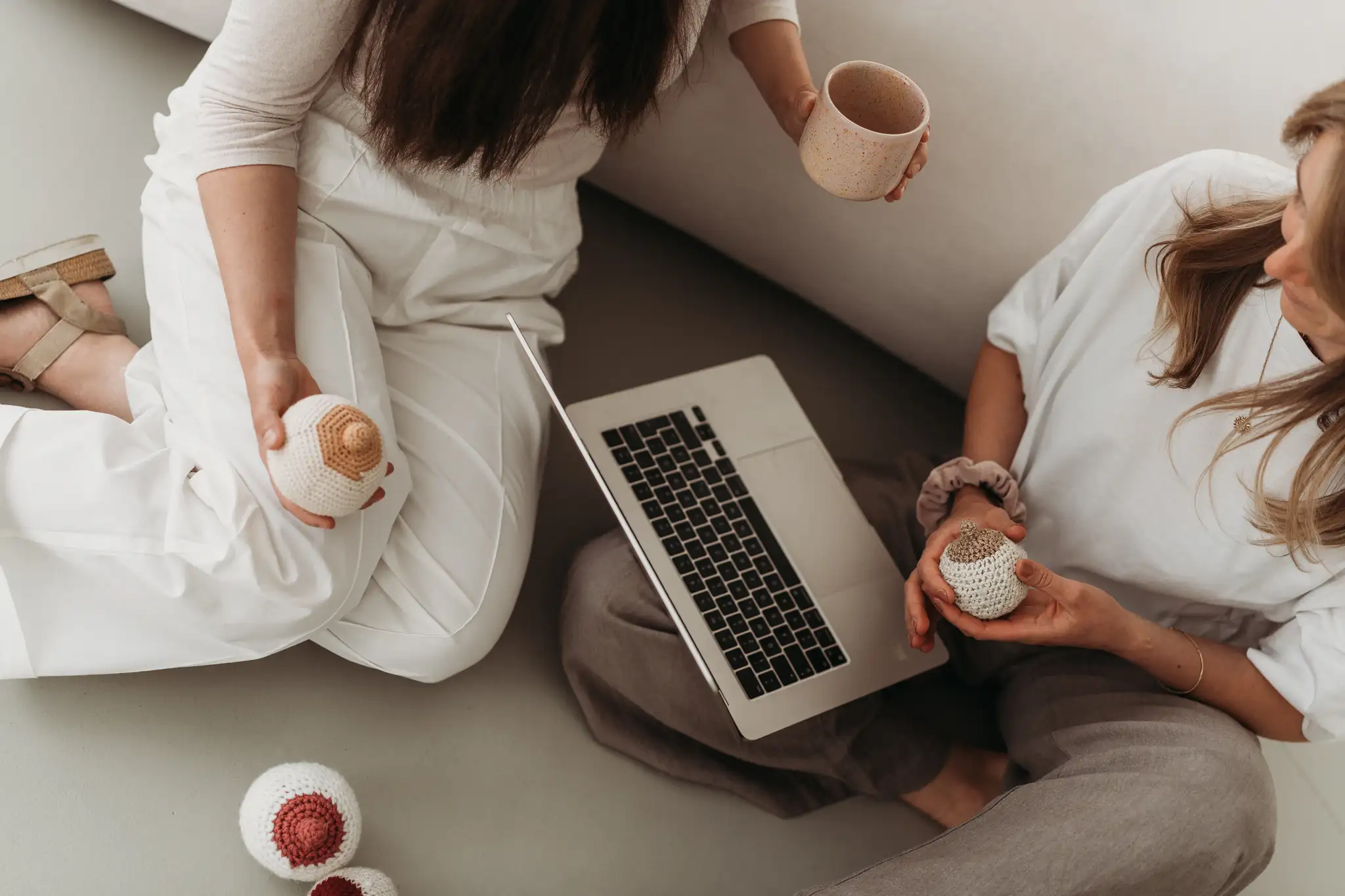Zwei Breastkeeperinnen im Austausch auf dem Sofa mit Laptop und gehäkeltem Brust-Modell – Zusammenarbeit im Breastkeeper Institut