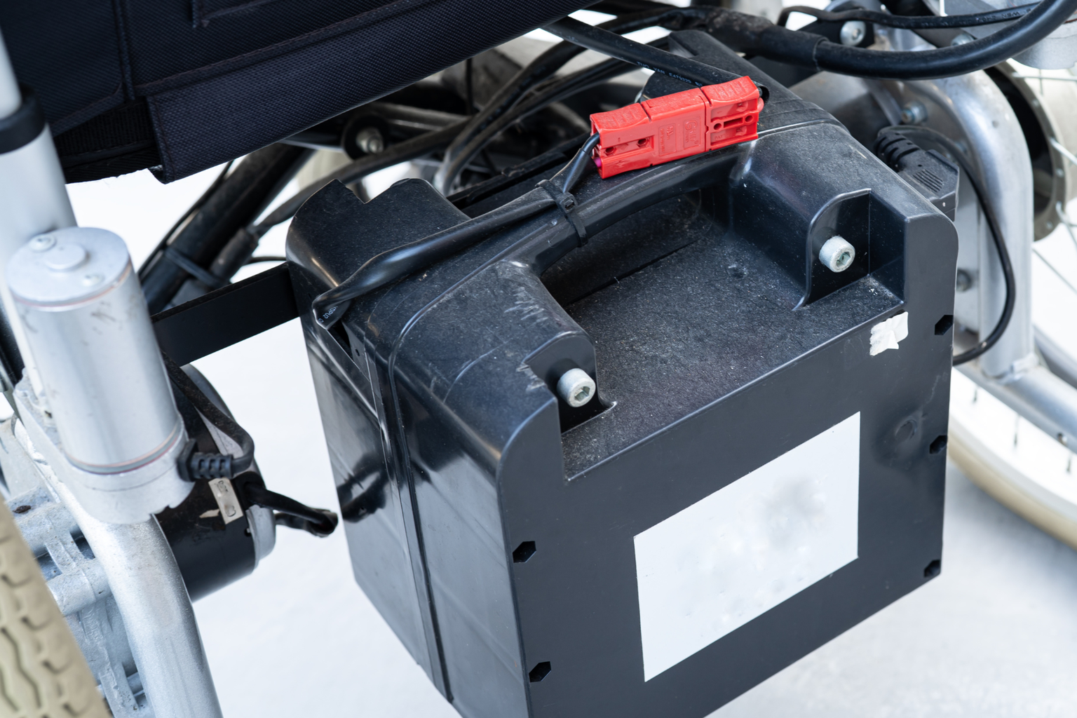 A close-up of a wheelchair battery pack attached to the wheelchair frame with visible cables and connectors.