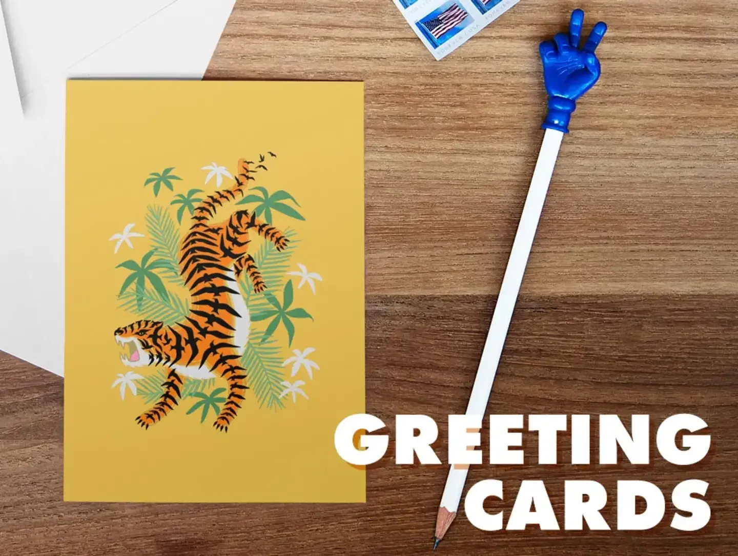Yellow greeting card with tiger illustration next to blue waving hand prop with 'Greeting Cards' text.