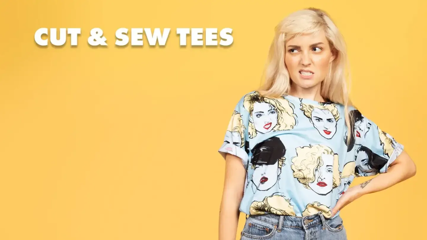 Blonde woman in light blue women's cut and sew t-shirt with pop-art faces print on yellow studio backdrop.