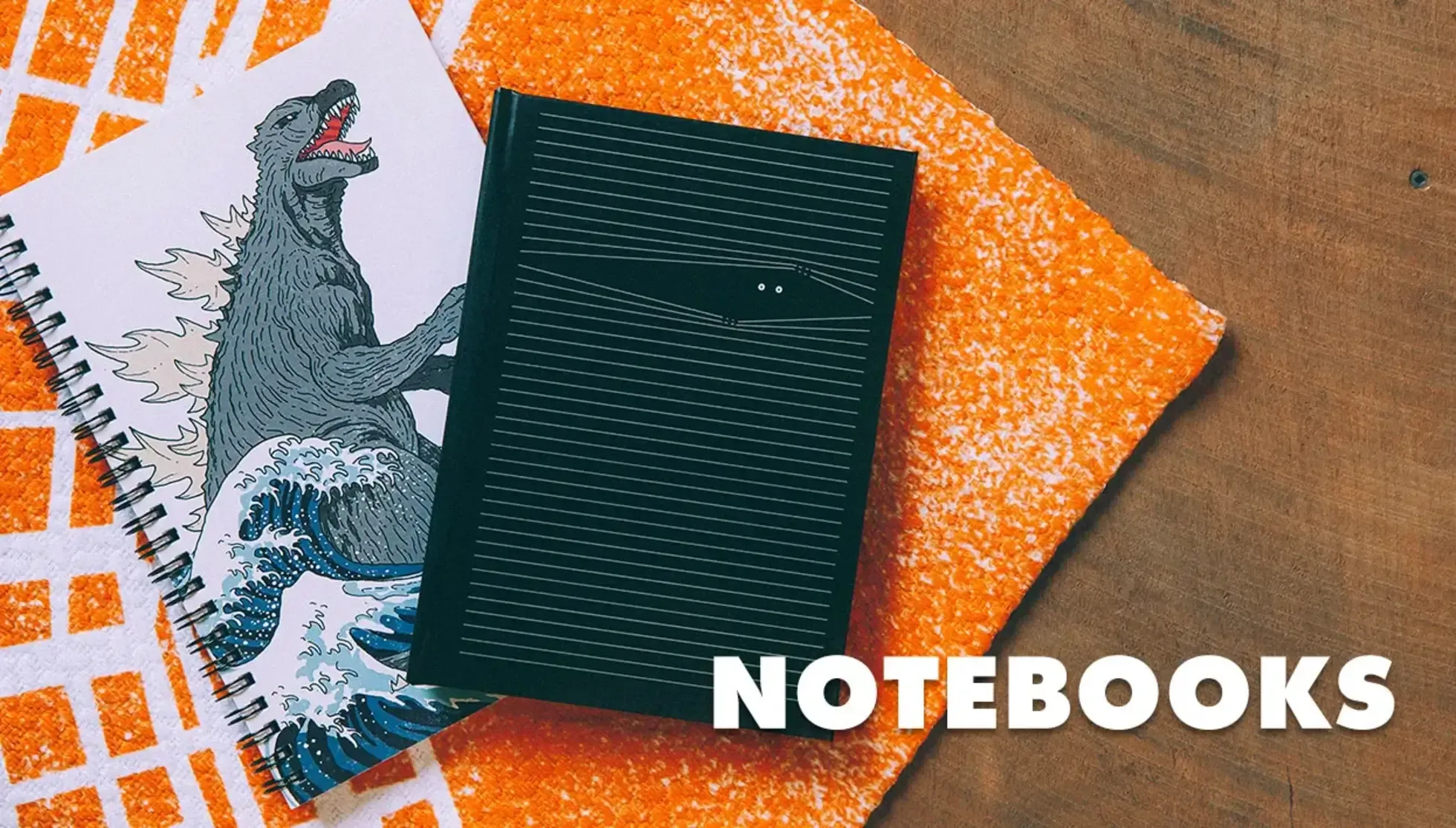 Closed black notebook on orange Godzilla print pouch with 'Notebooks' text.