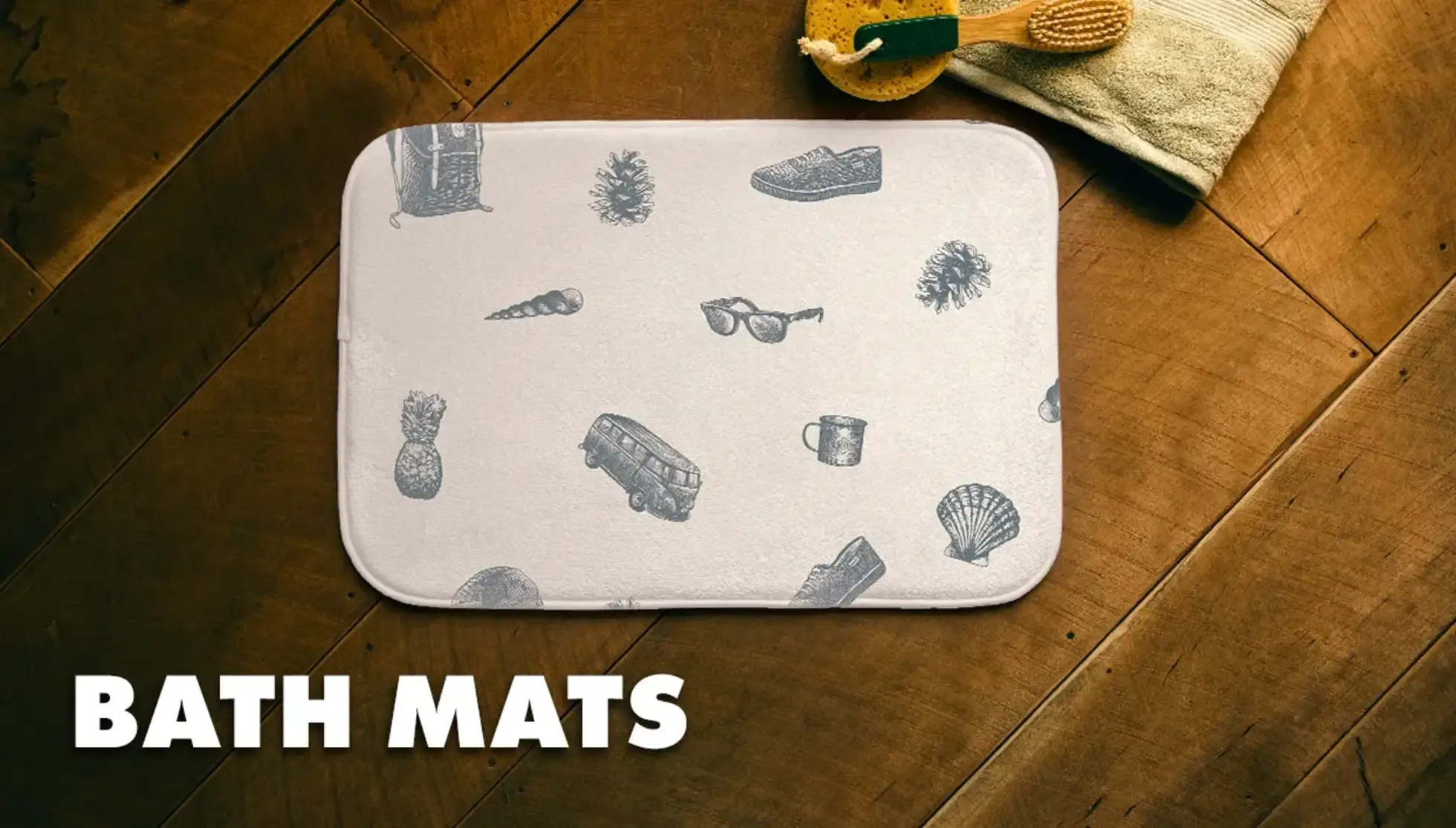 Beige bath mat with travel doodles next to yellow towel on dark wood floor labelled 'Bath Mats'.
